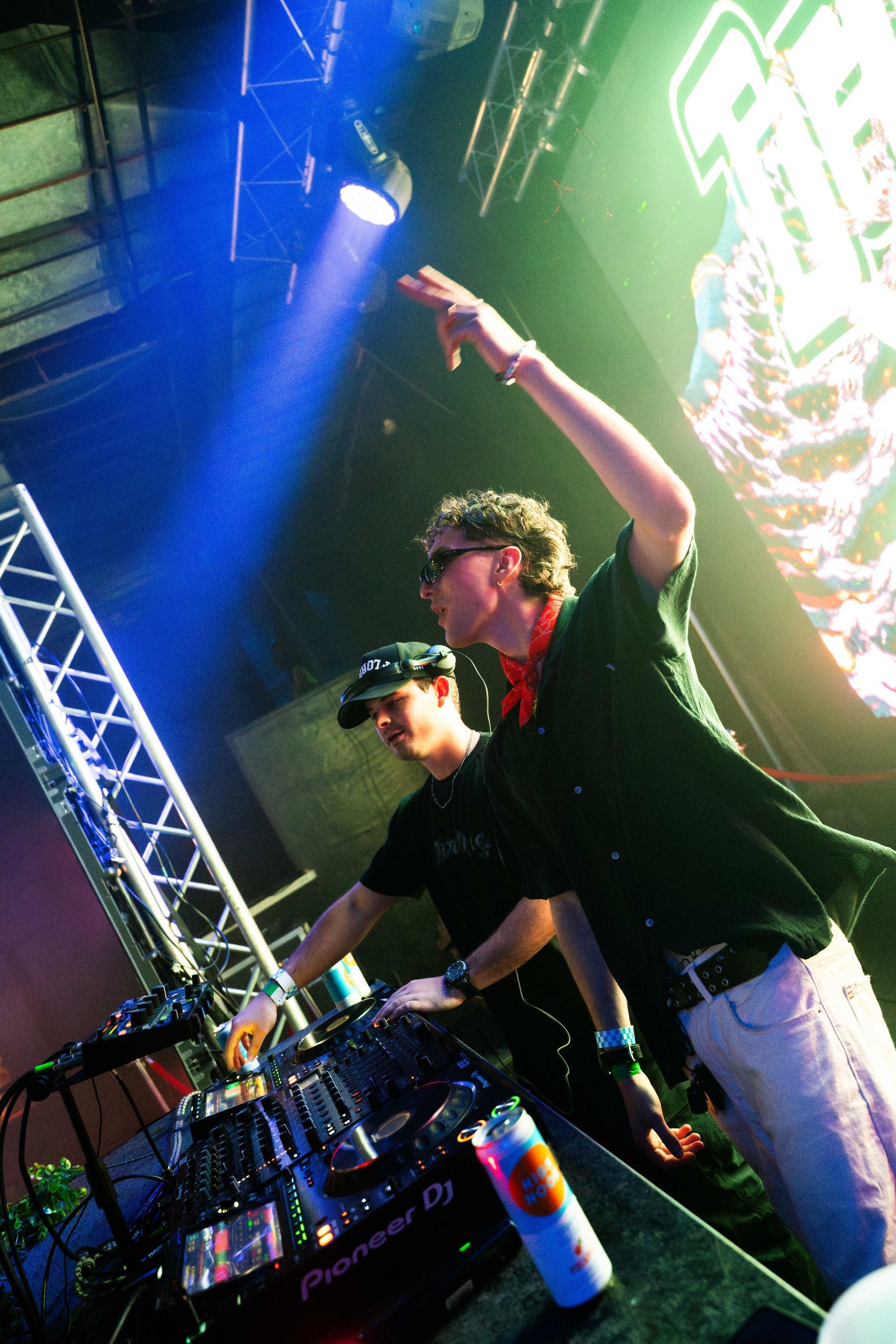 Two men are playing music on a stage with a can of red bull in front of them