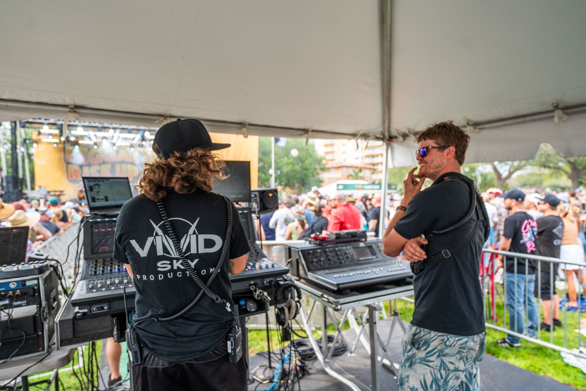 Two men are standing in front of a crowd under a tent.