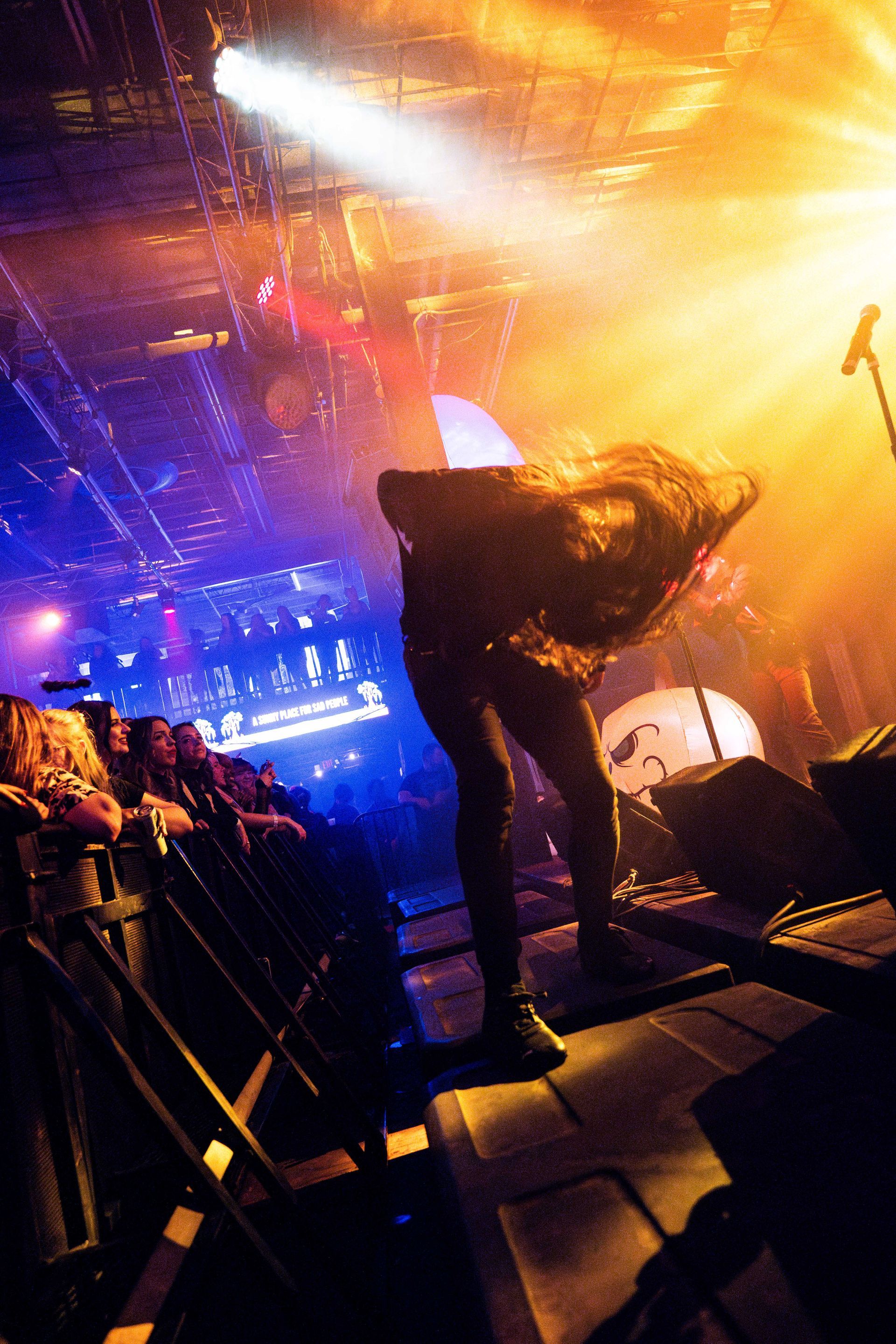 A man is standing on a stage in front of a crowd playing a guitar.