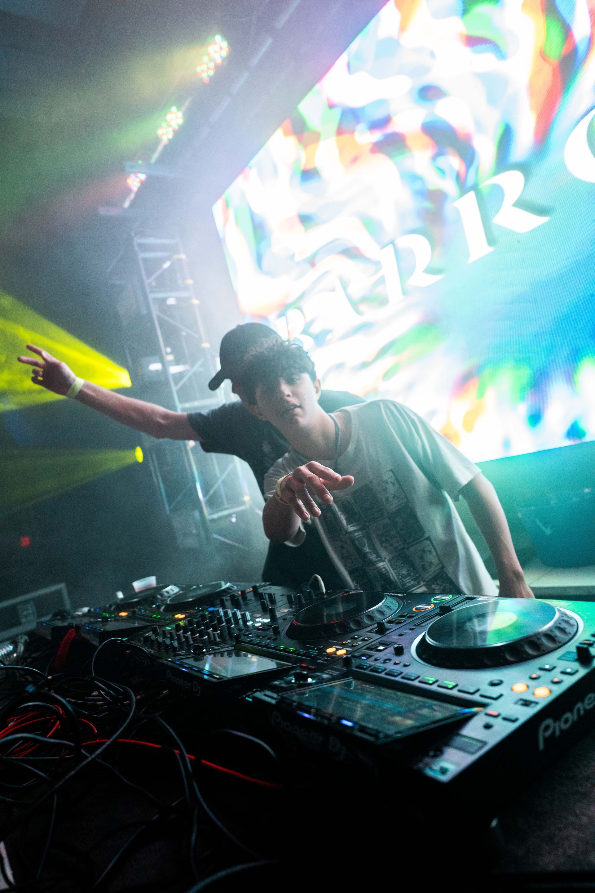 A man is standing in front of a dj mixer in a dark room.