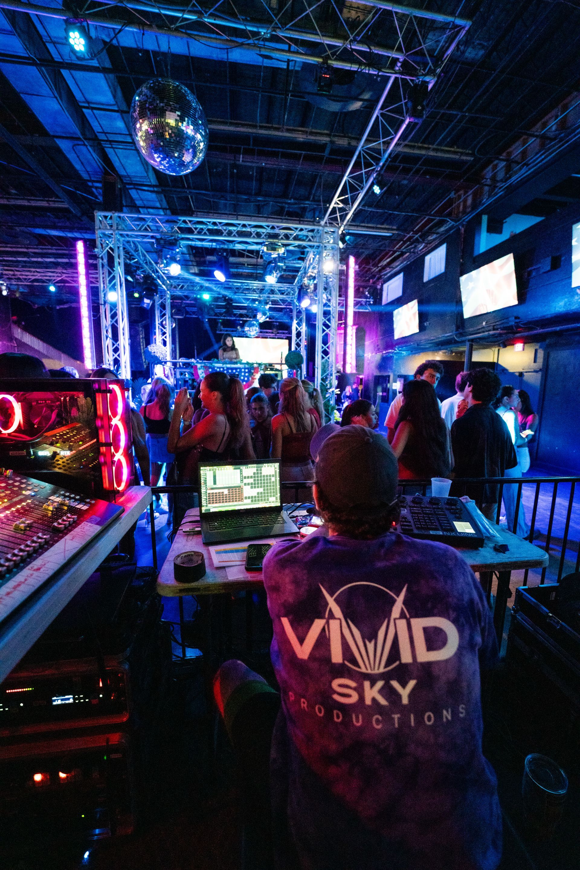 A man is sitting in front of a laptop in a club.