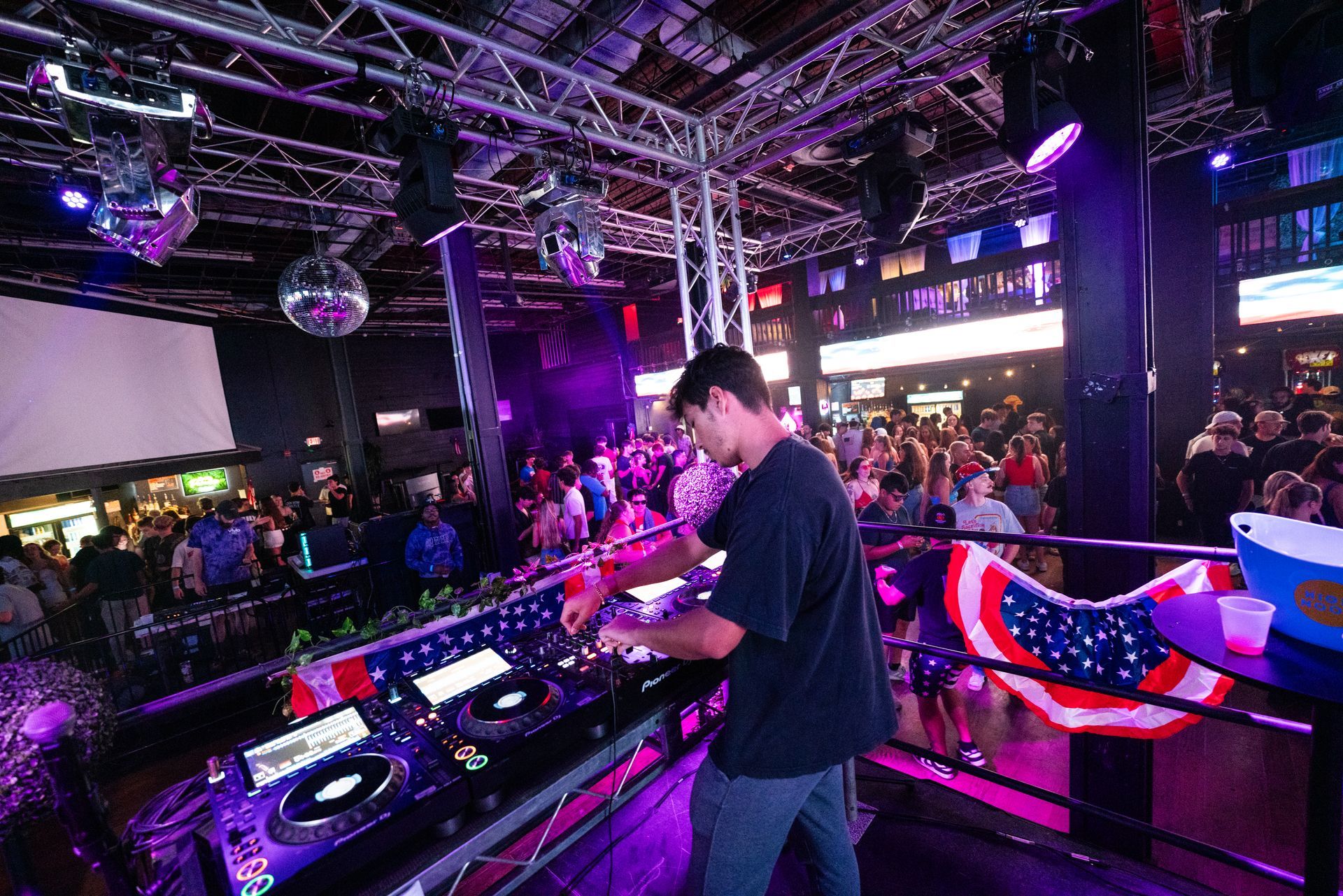 A man is standing in front of a dj booth in a club.