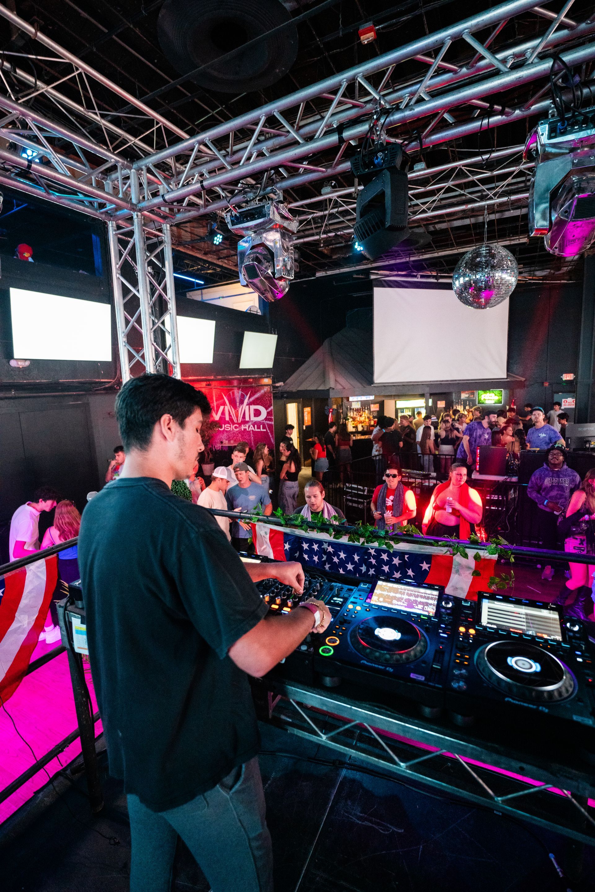 A man is standing in front of a dj booth in a club.