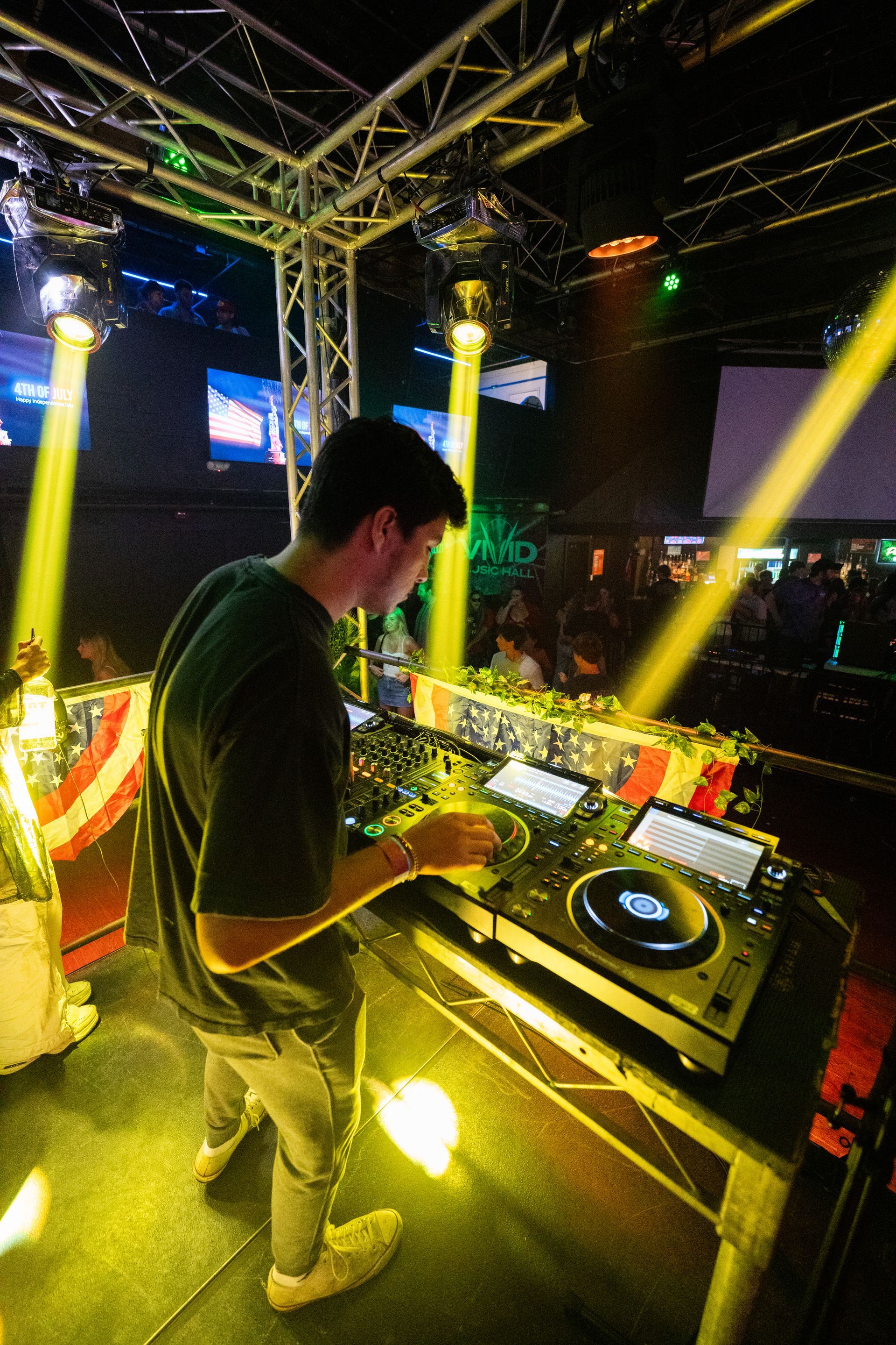 A man is standing in front of a dj booth in a club.
