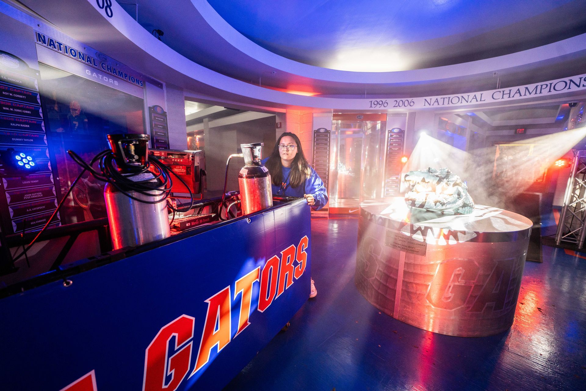 A woman is standing in front of a gators sign in a dark room.