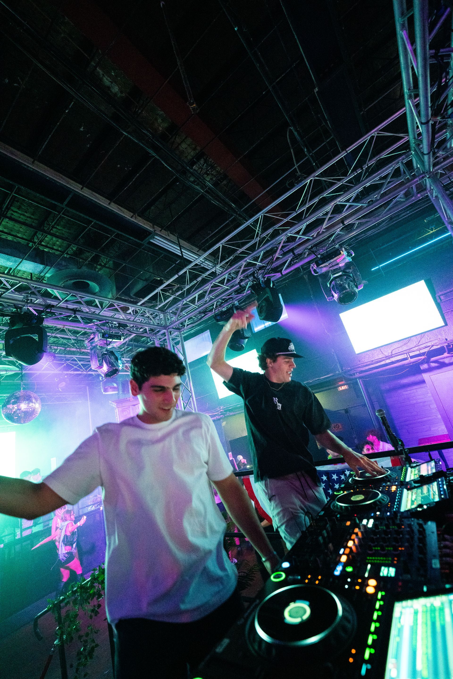 Two men are playing music on a stage in a club.