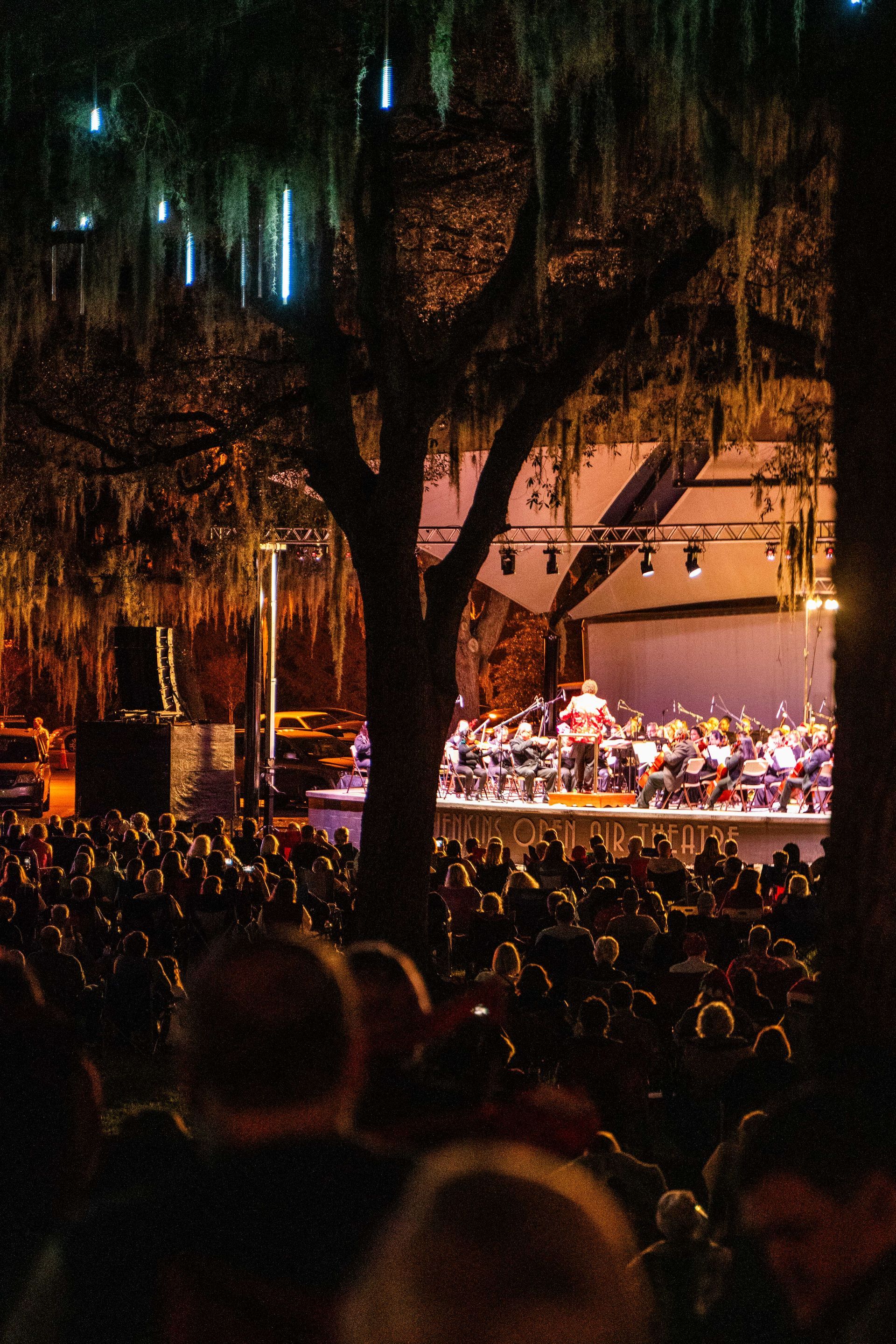 A crowd of people watching an orchestra perform on a stage at night