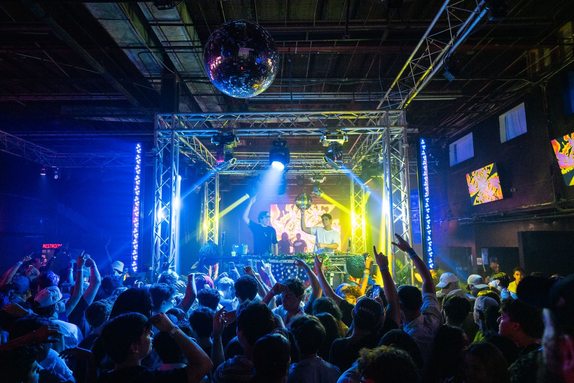 A crowd of people are dancing in a club with a disco ball hanging from the ceiling.