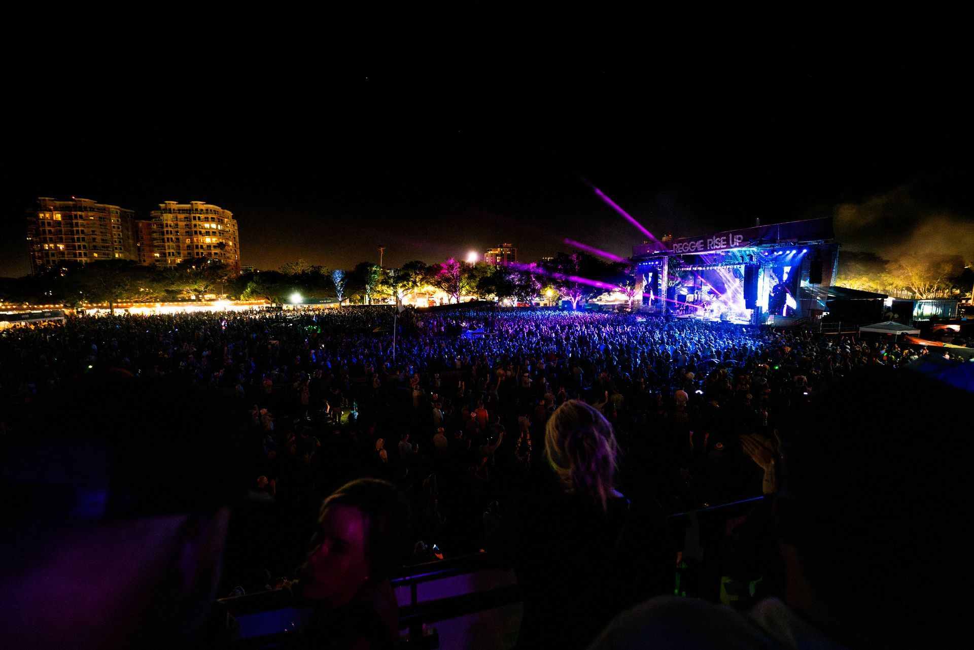 A large crowd of people are watching a concert at night.
