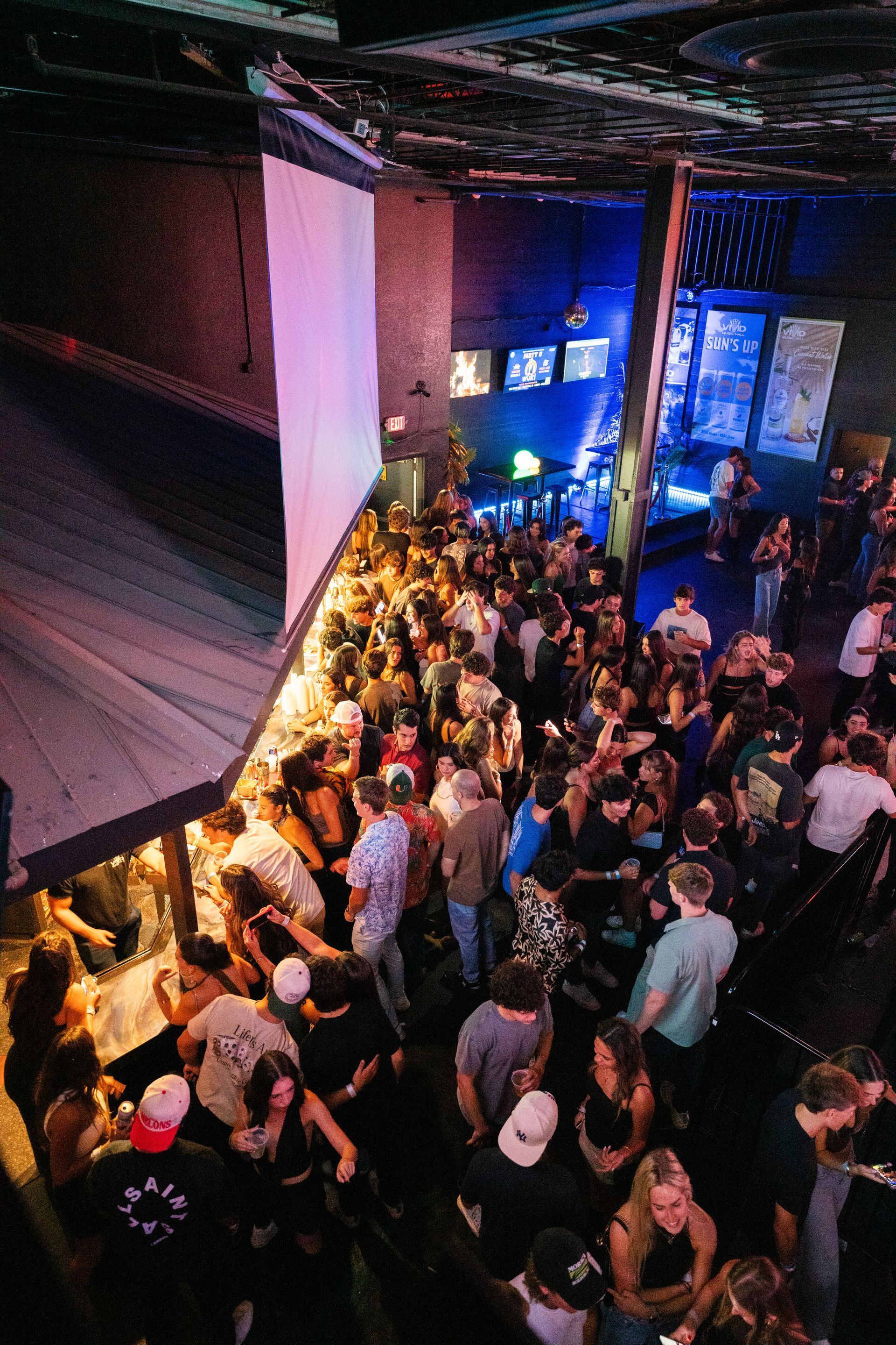 A large crowd of people are gathered in a dark room at a party.