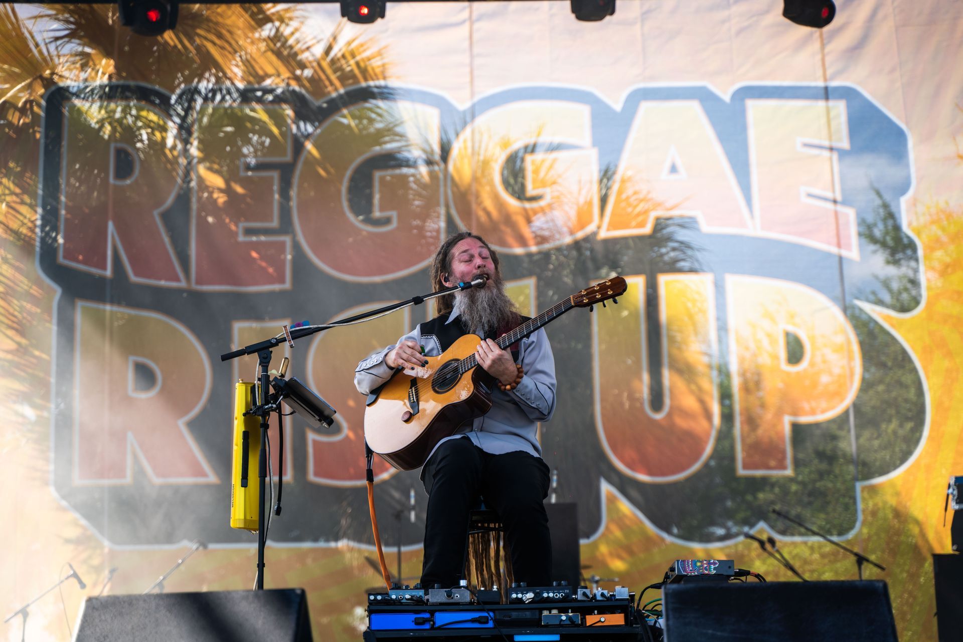 A man singing into a microphone while playing a guitar in front of a sign that says reggae rest up