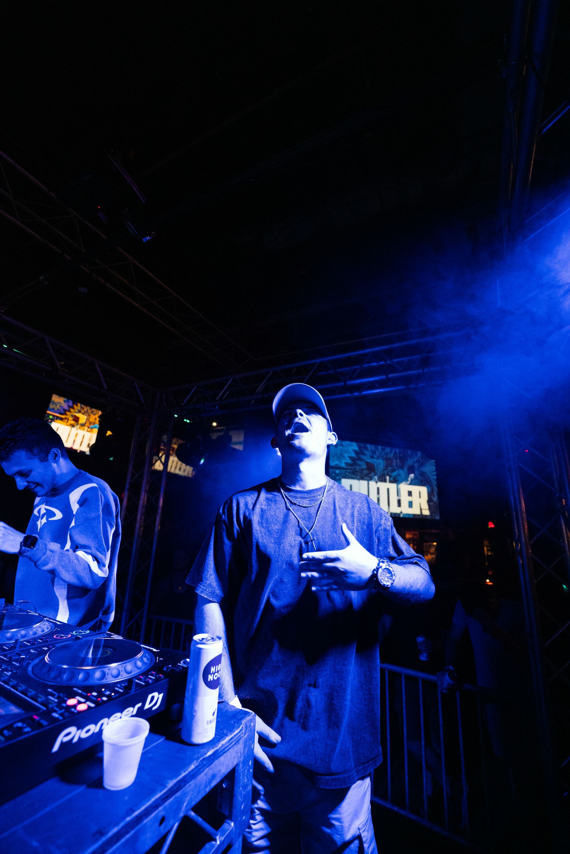 A man is standing in front of a dj mixer in a dark room.