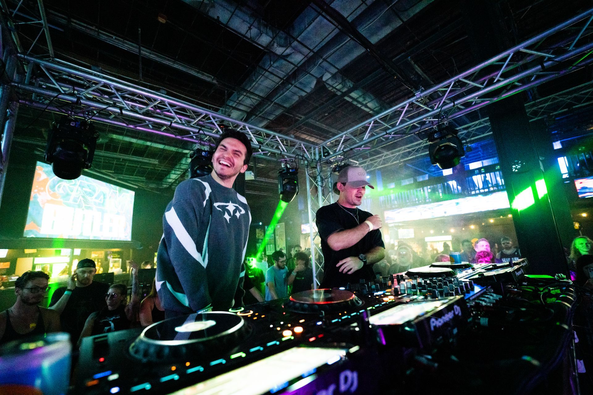 Two men are standing in front of a dj mixer in a club.