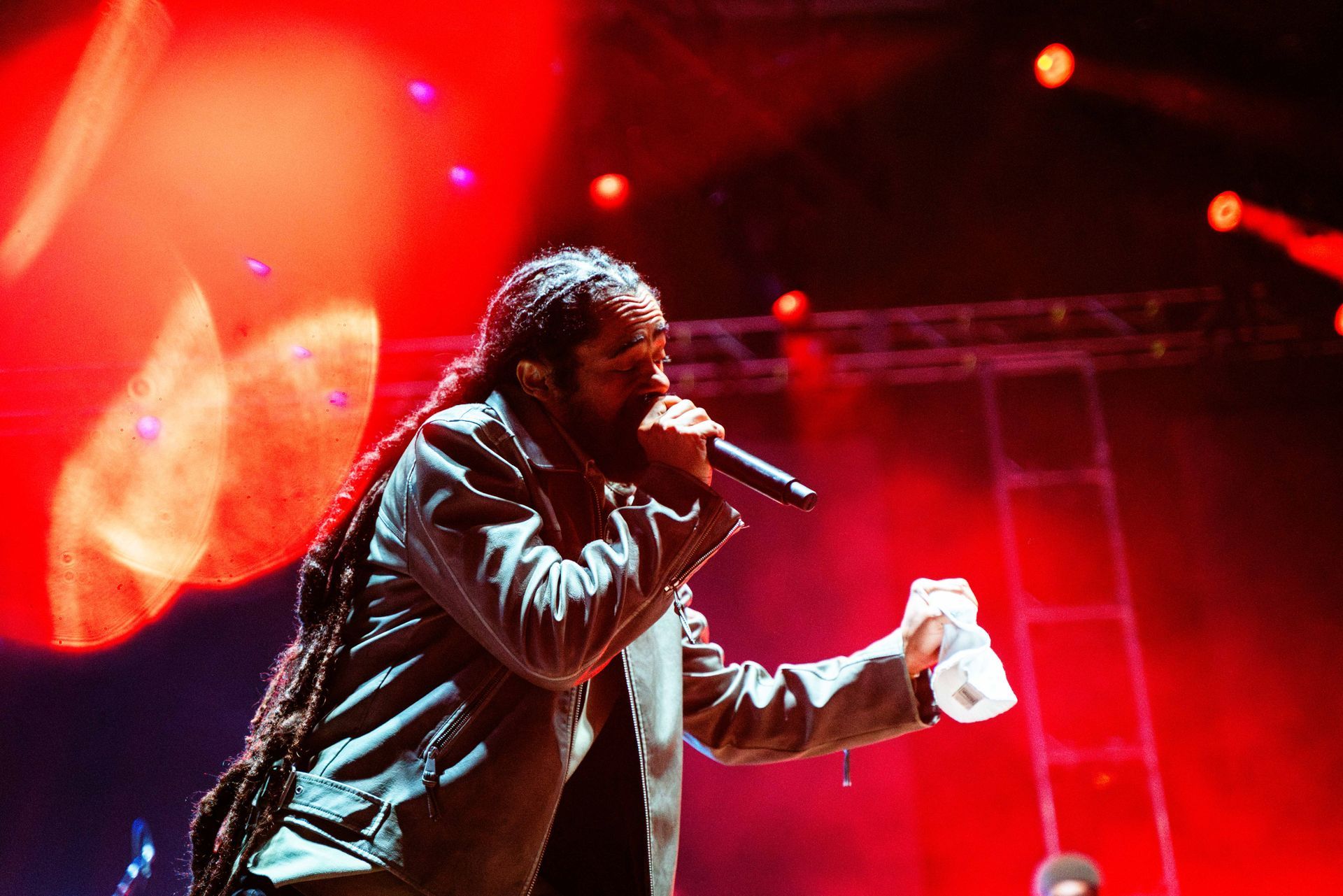 A man with dreadlocks is singing into a microphone on a stage.