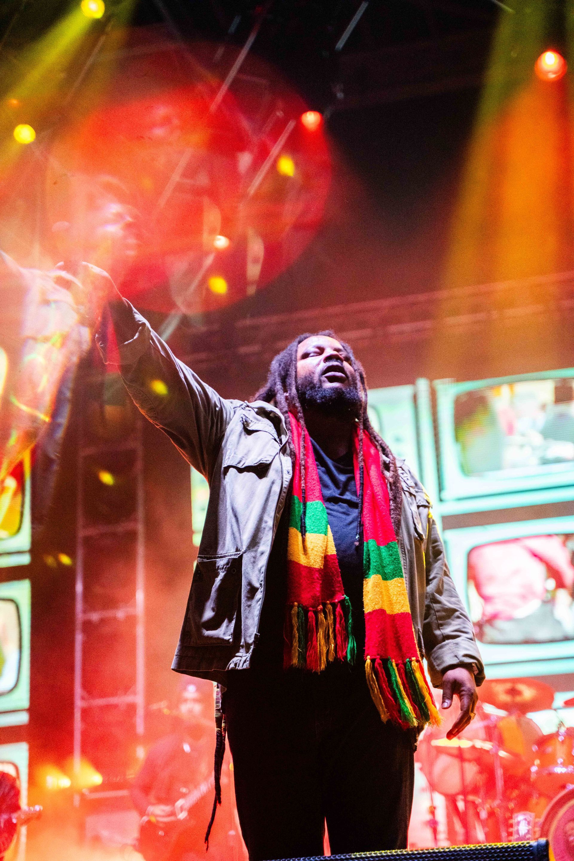 A man with dreadlocks is singing into a microphone on a stage
