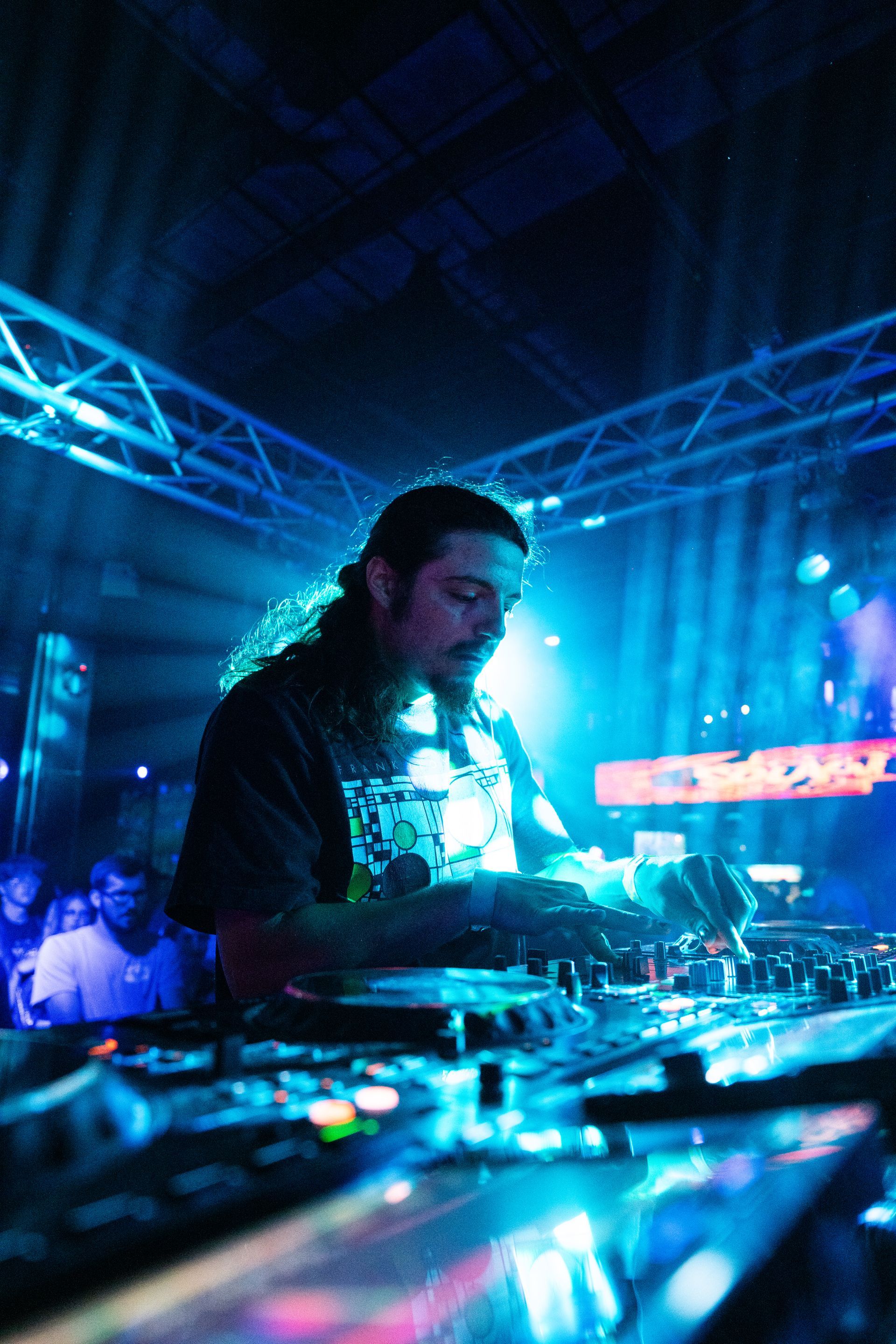 A man with long hair is playing a dj set in a dark room