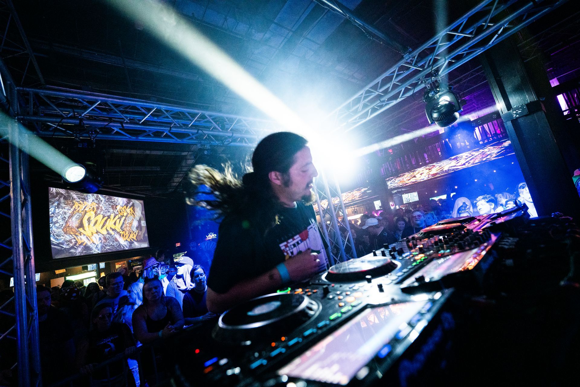A dj is playing music in front of a crowd in a dark room.