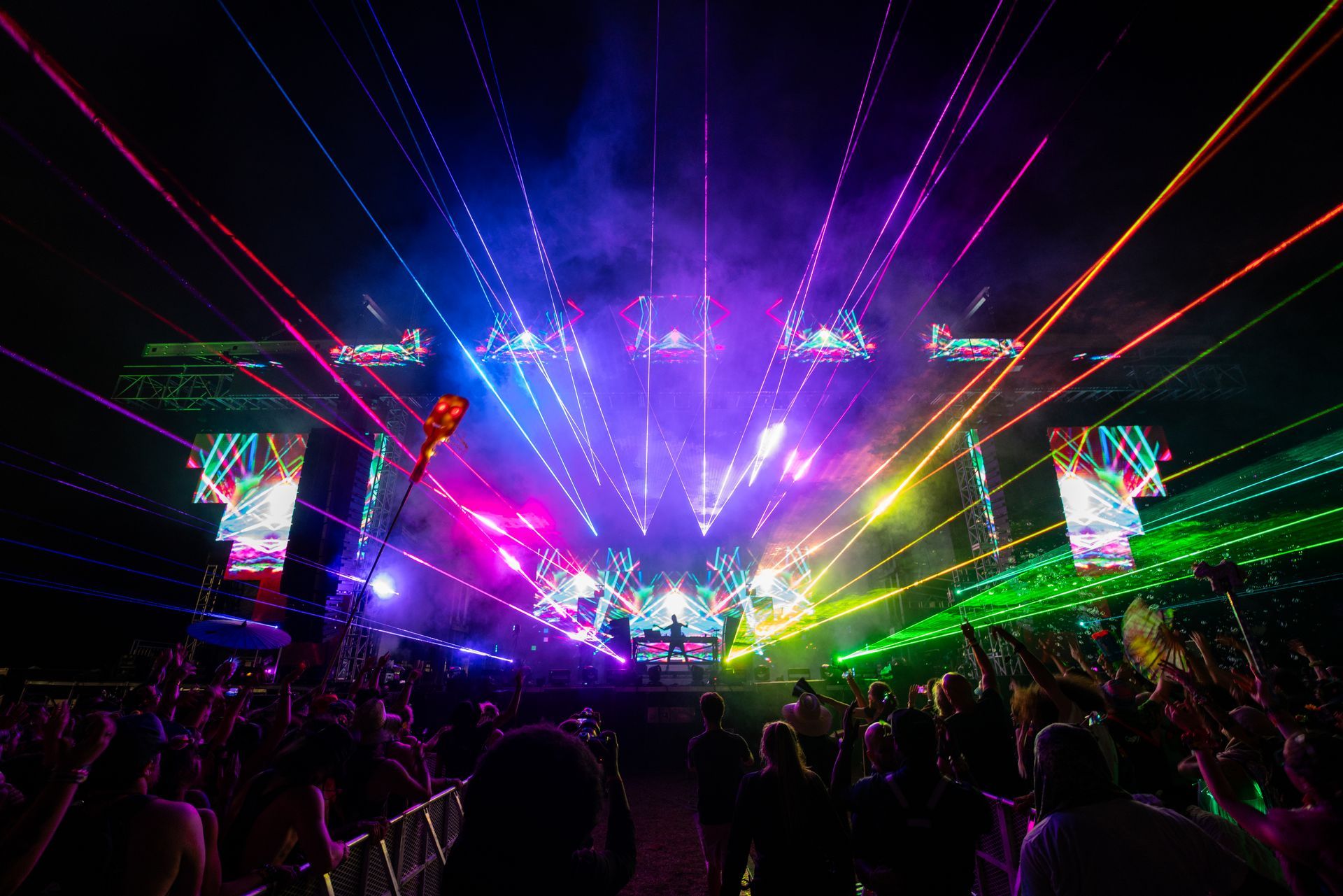 A crowd of people are watching a concert with a lot of lights coming out of the stage.