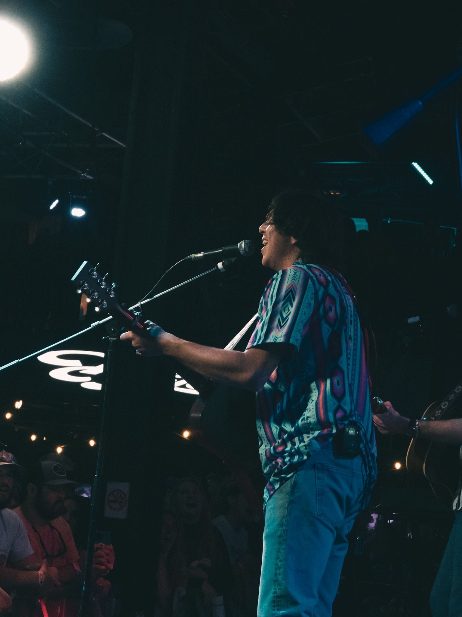 A man is playing a guitar and singing into a microphone on a stage.