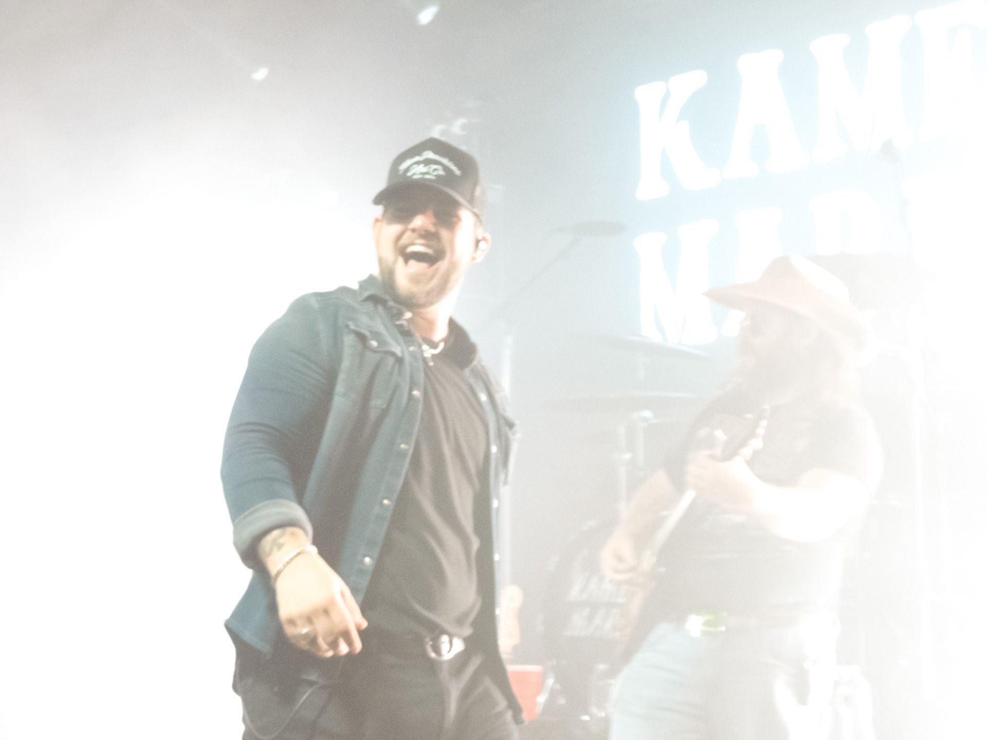 A man is singing on stage in front of a sign that says kam
