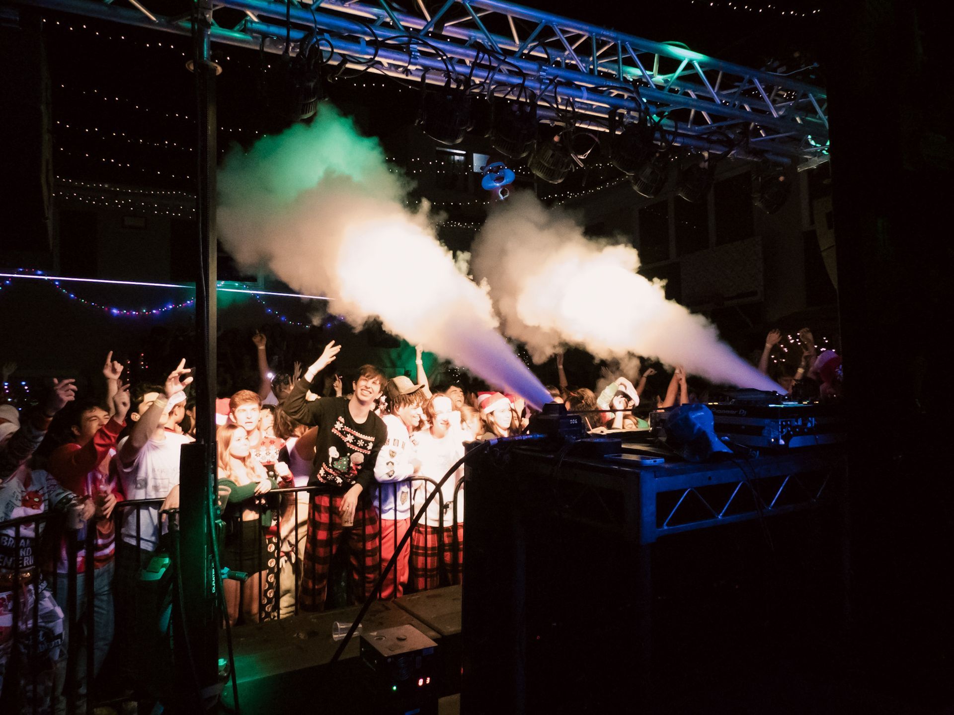 A crowd of people are standing in front of a stage with smoke coming out of it.