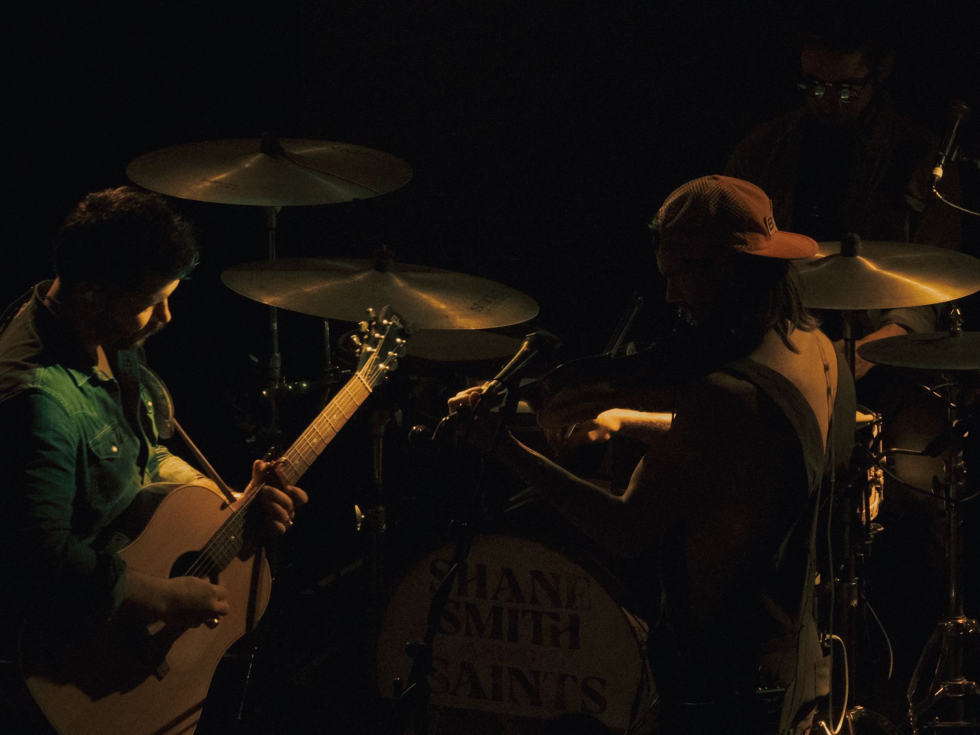 A man playing a guitar in front of a drum set that says shane smith saints