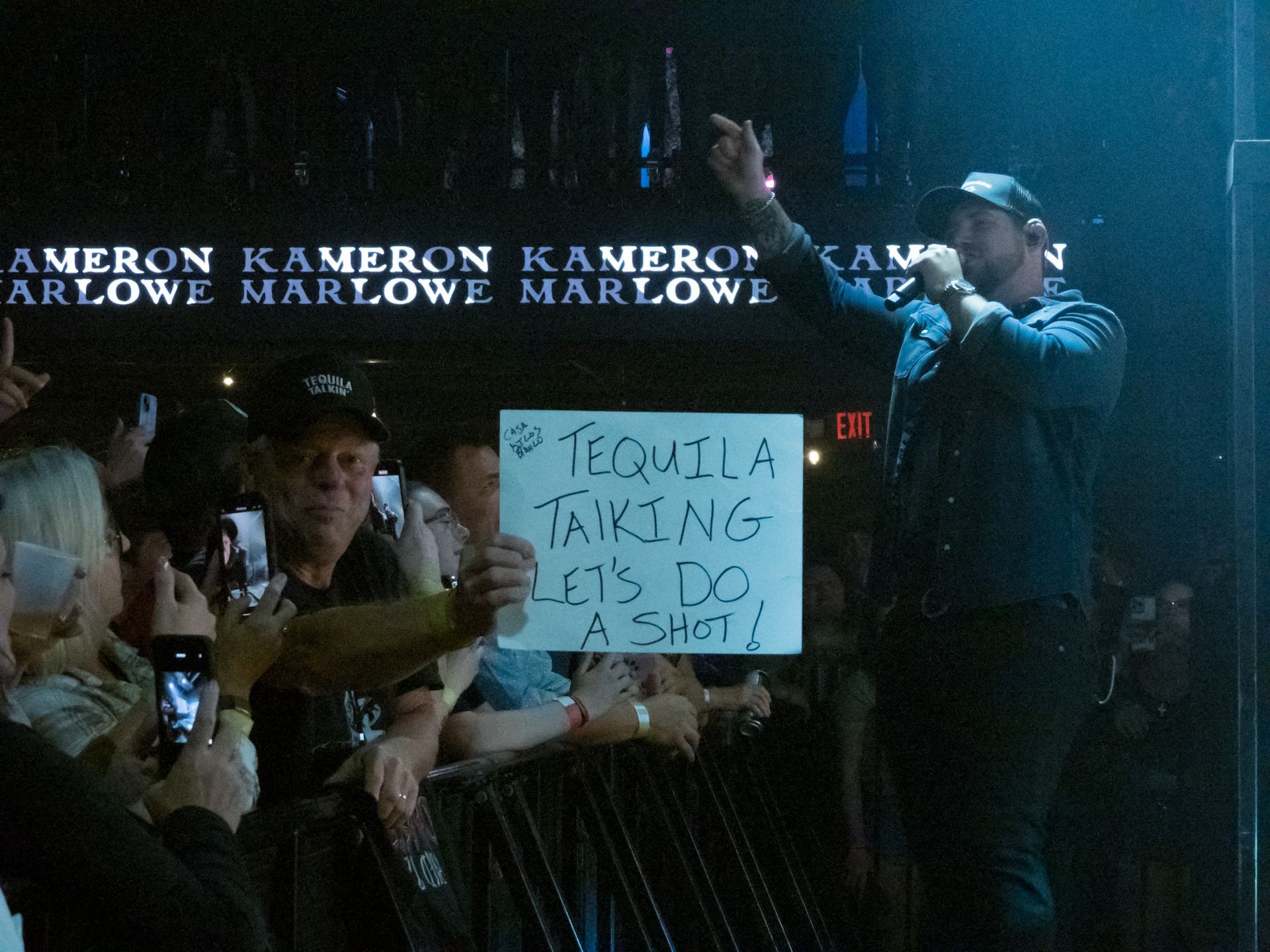 A man holding a sign that says tequila talking lets do a shot