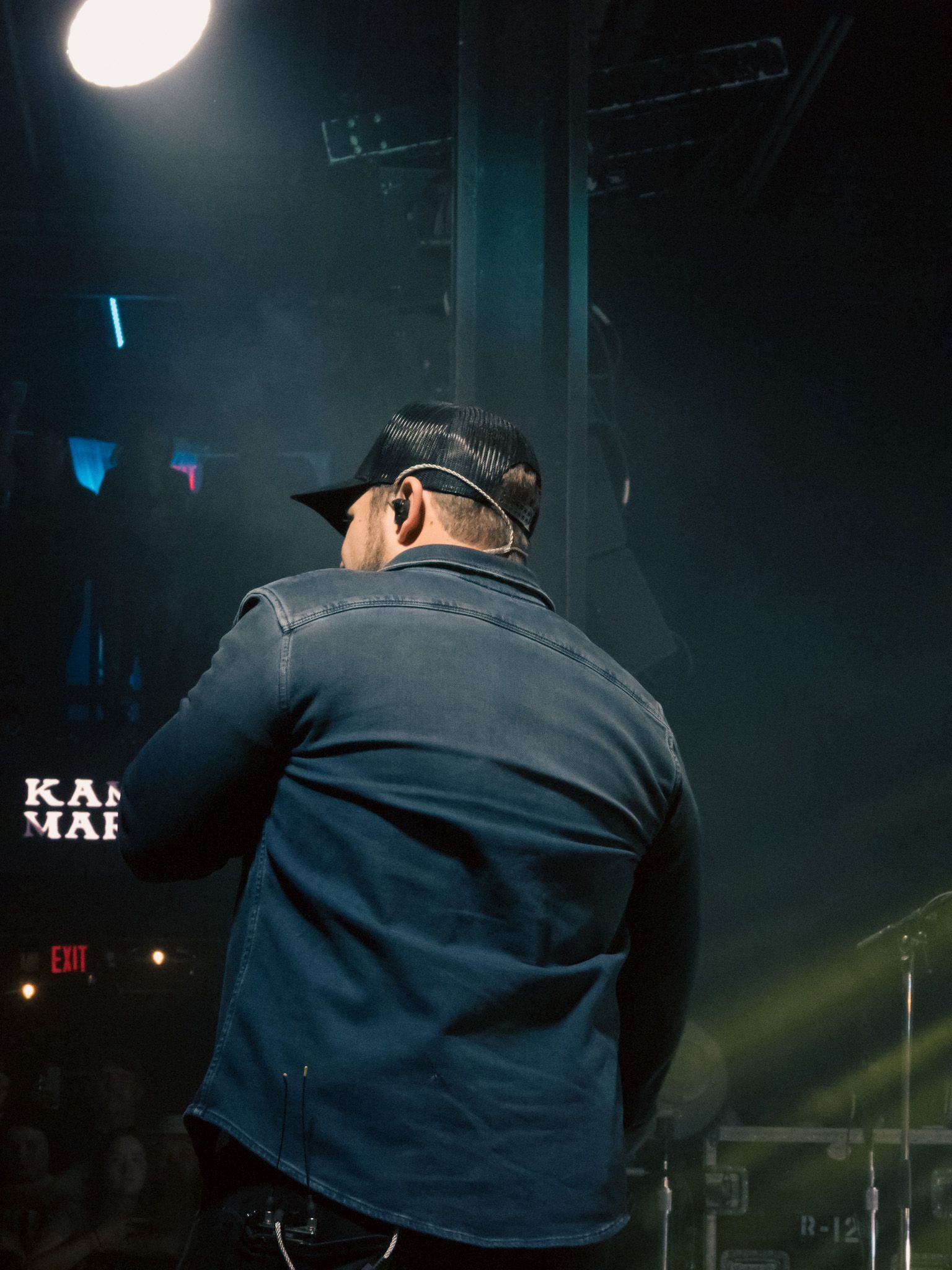 A man wearing a hat and ear buds is singing into a microphone on a stage.
