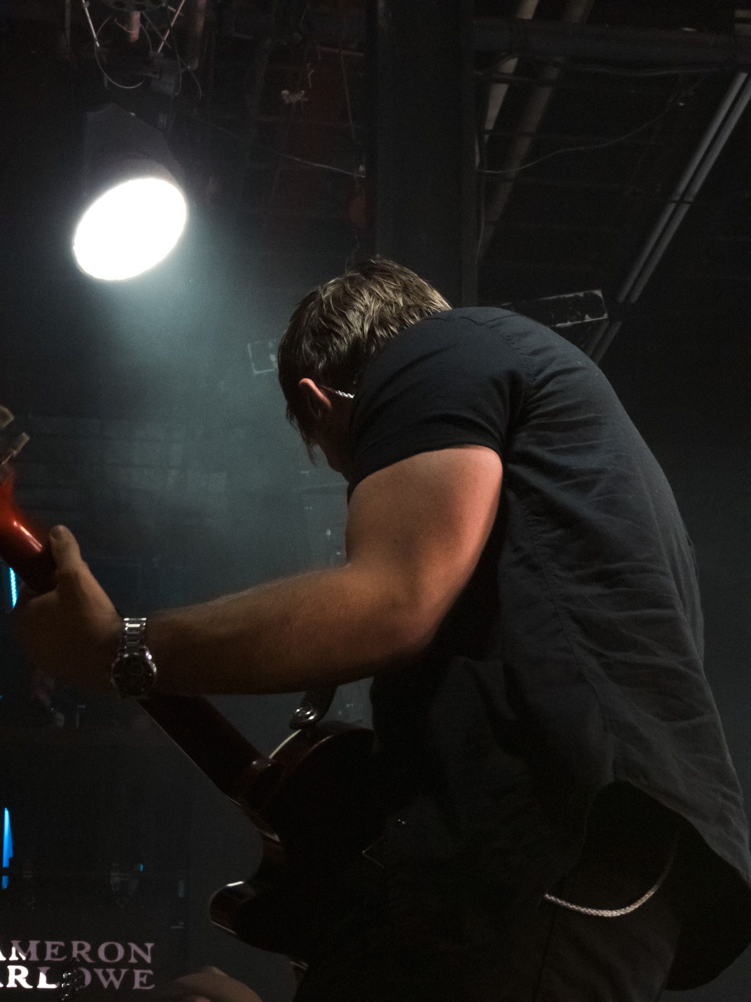 A man in a black shirt is playing a guitar in a dark room