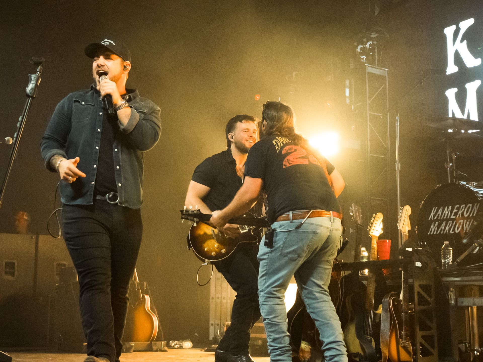 A man singing into a microphone while two other men play guitars on stage