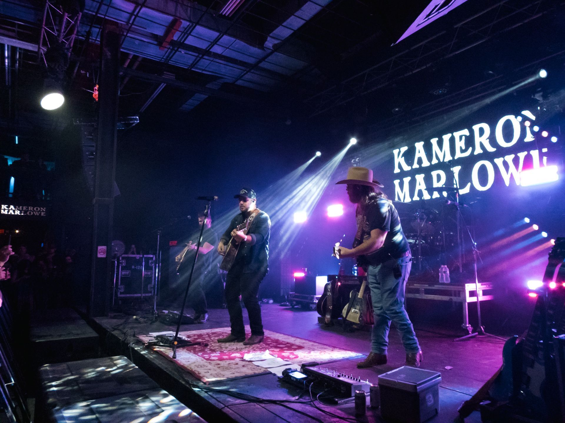 A group of men are playing guitars on a stage in front of a sign that says kameron maplowe.