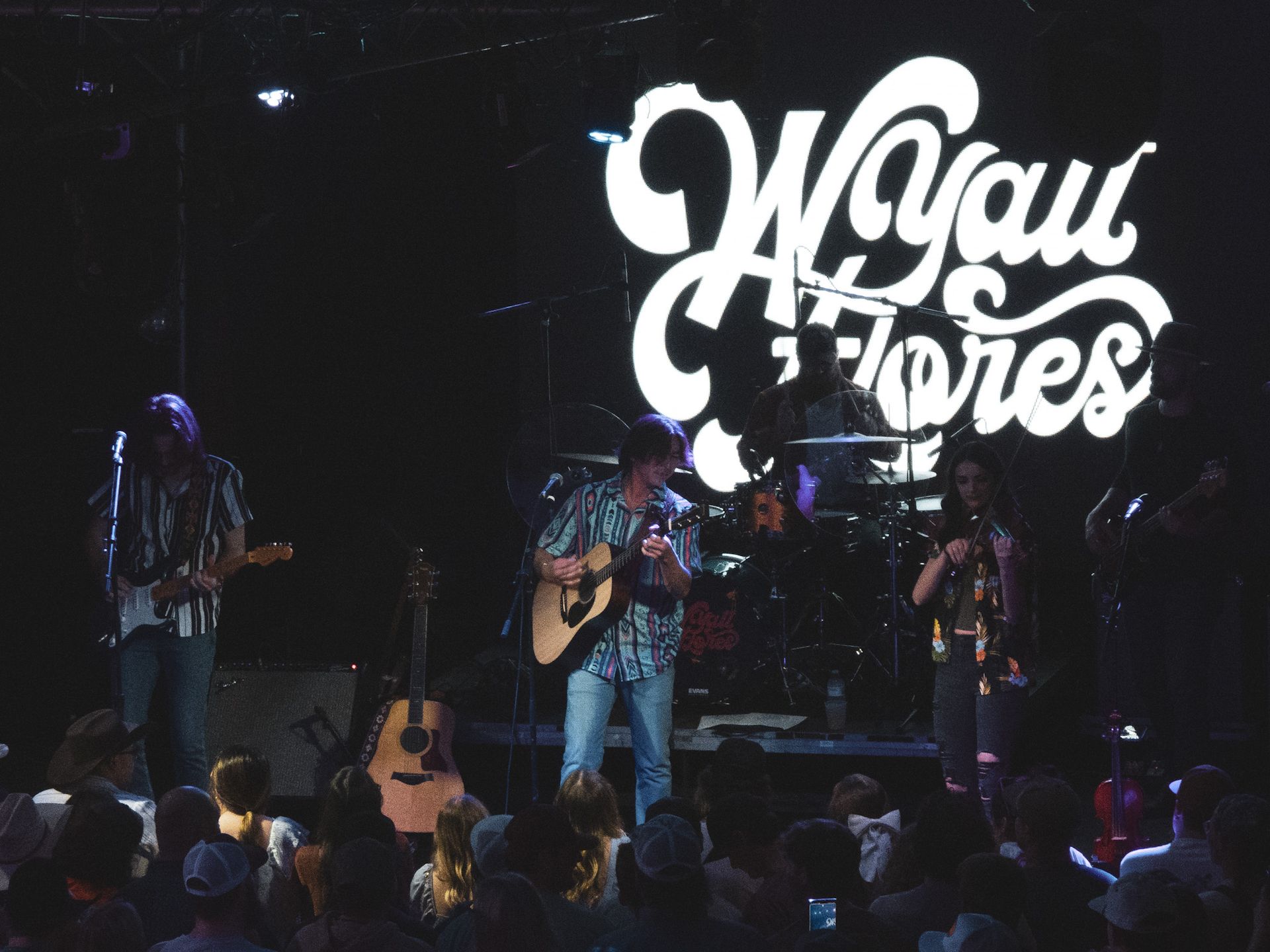 A man playing a guitar in front of a sign that says wgau flores