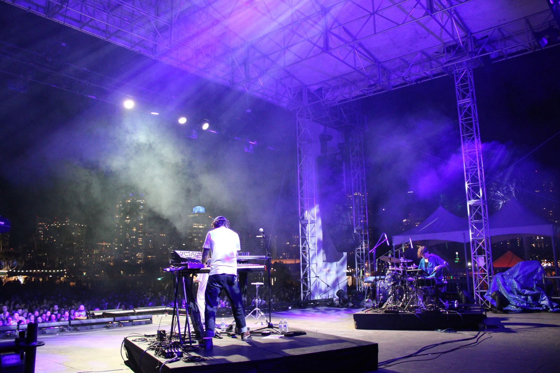 A man playing a keyboard on a stage with purple lights