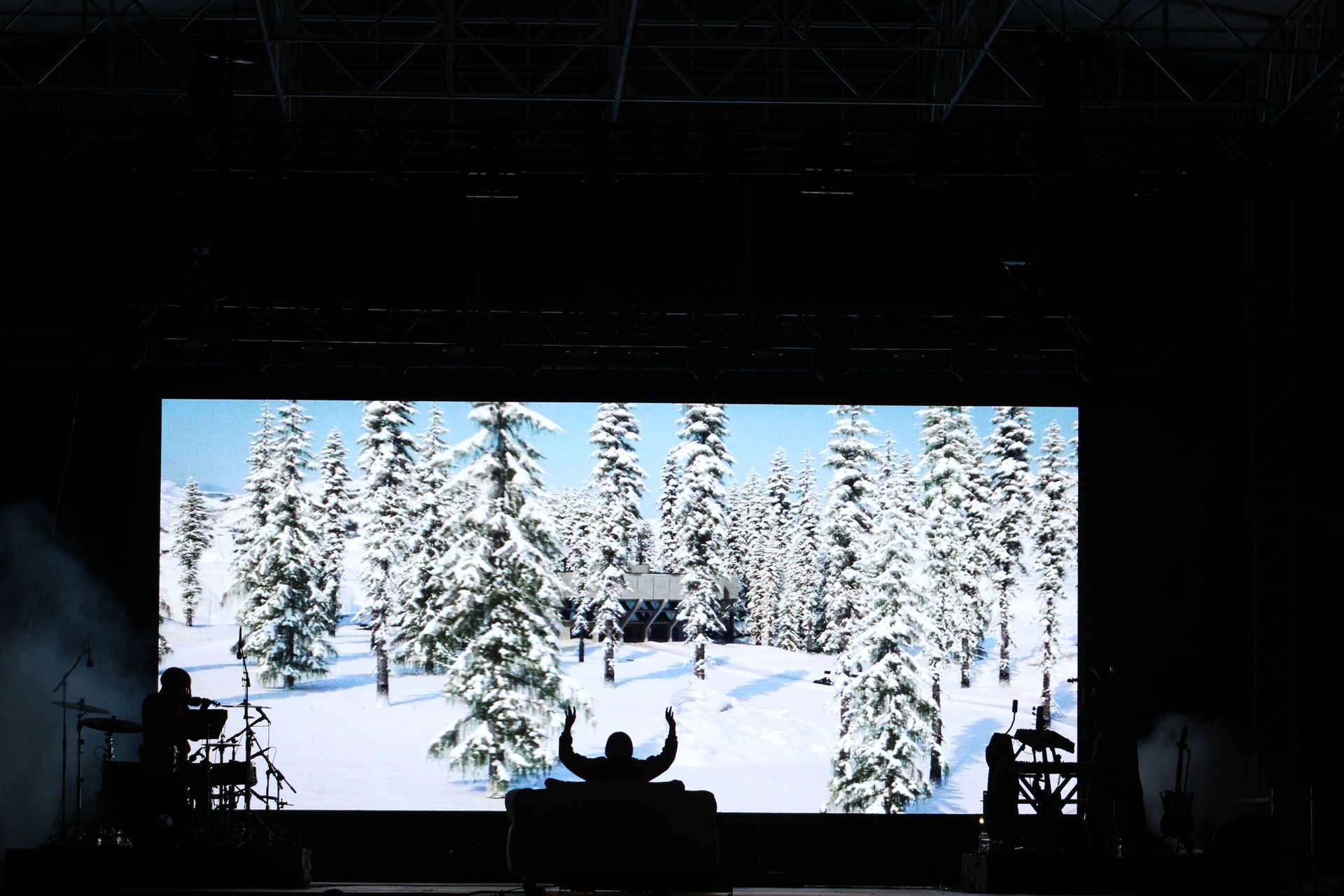 A man is standing in front of a large screen with a snowy forest on it.