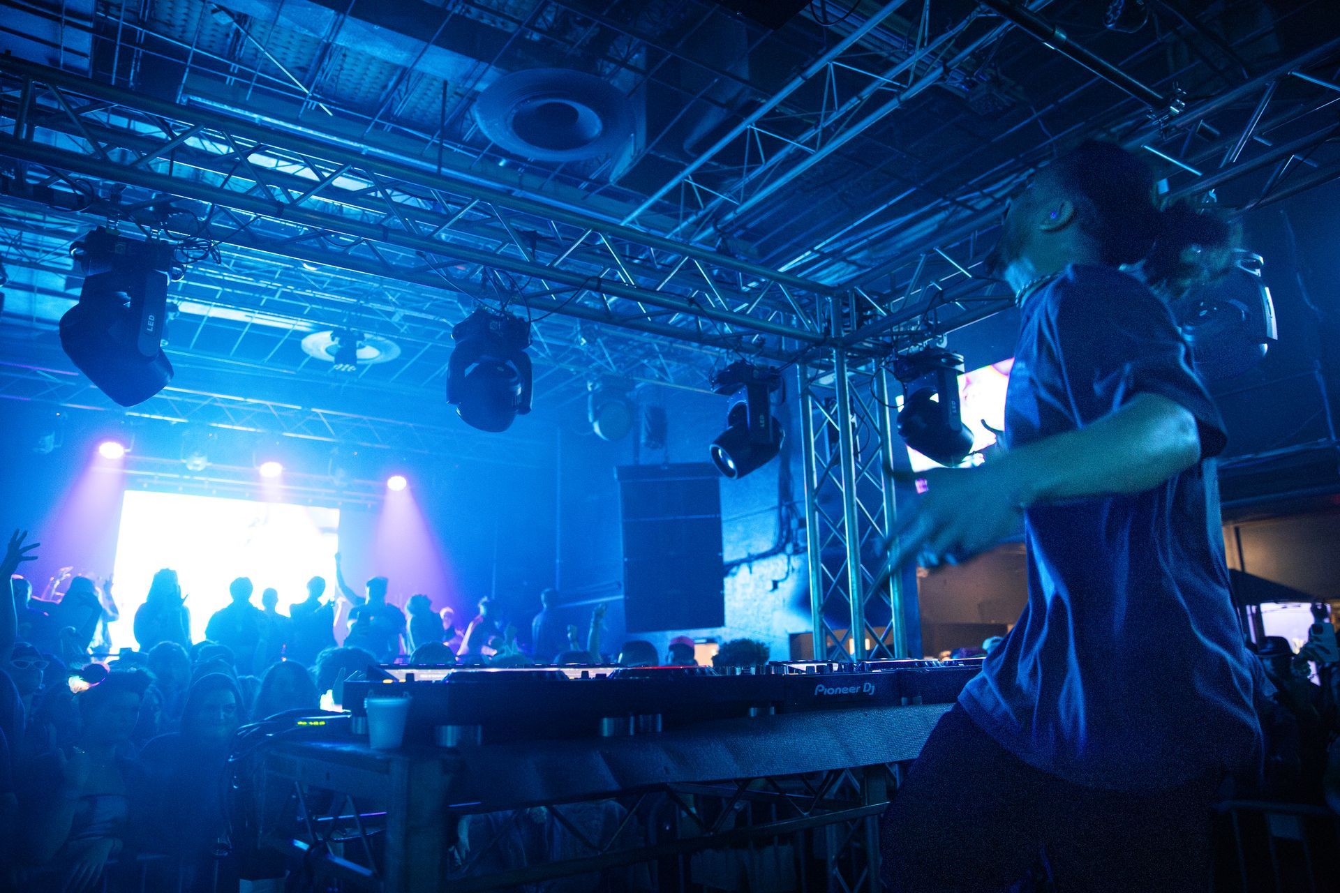 A man in a blue shirt is playing a dj set in a dark room