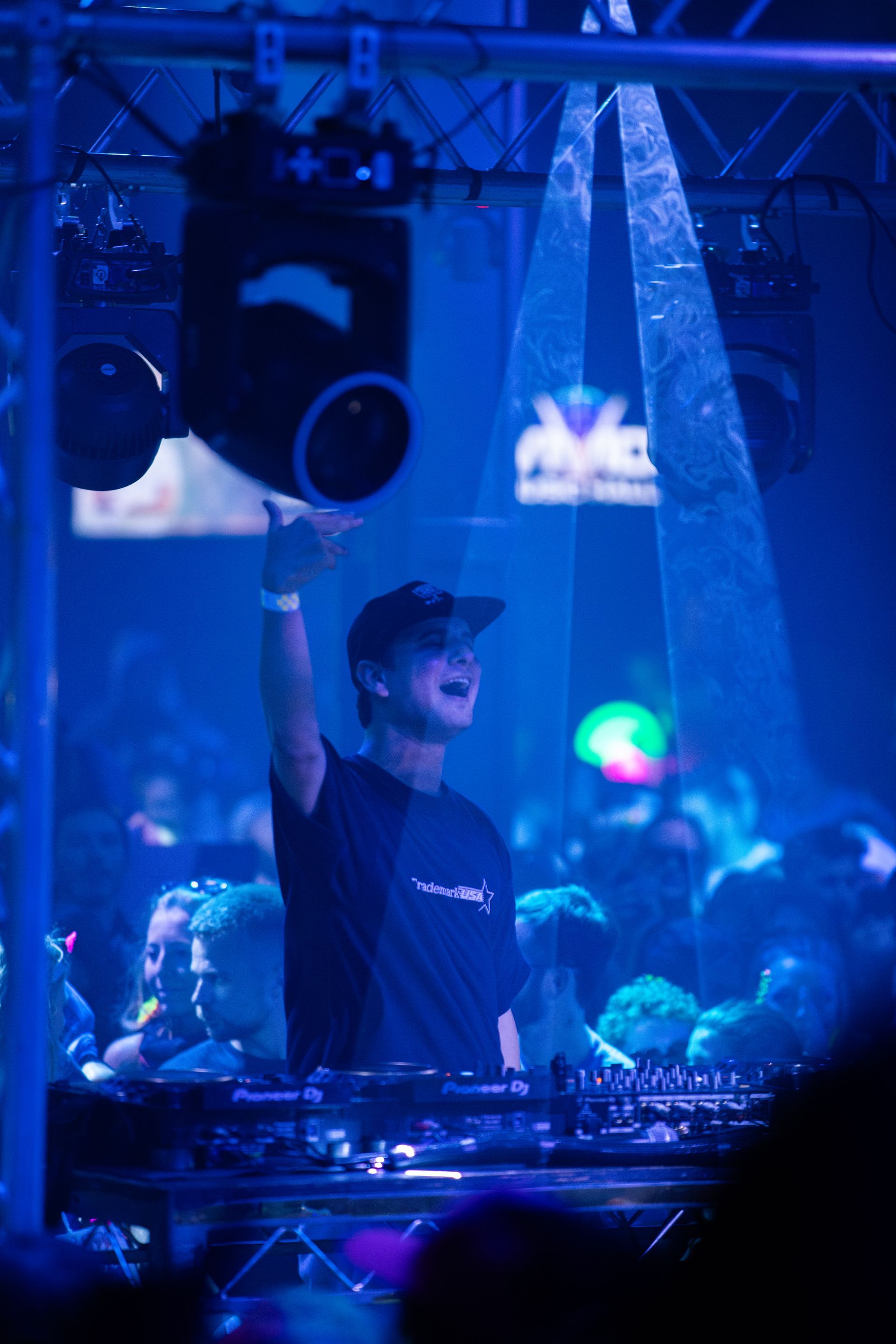 A man is standing in front of a crowd in a dark room with his arms in the air.