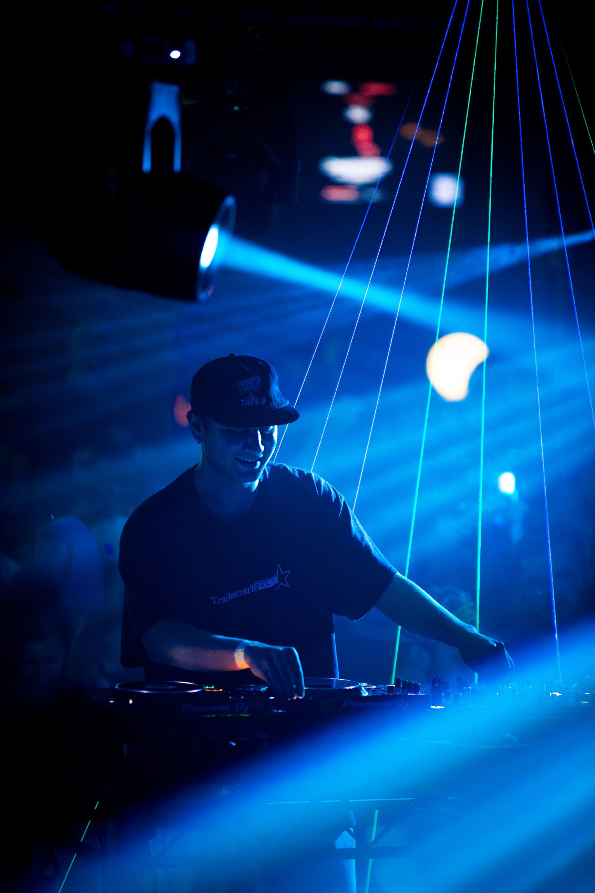 A man is playing a dj set in a dark room with blue lights behind him