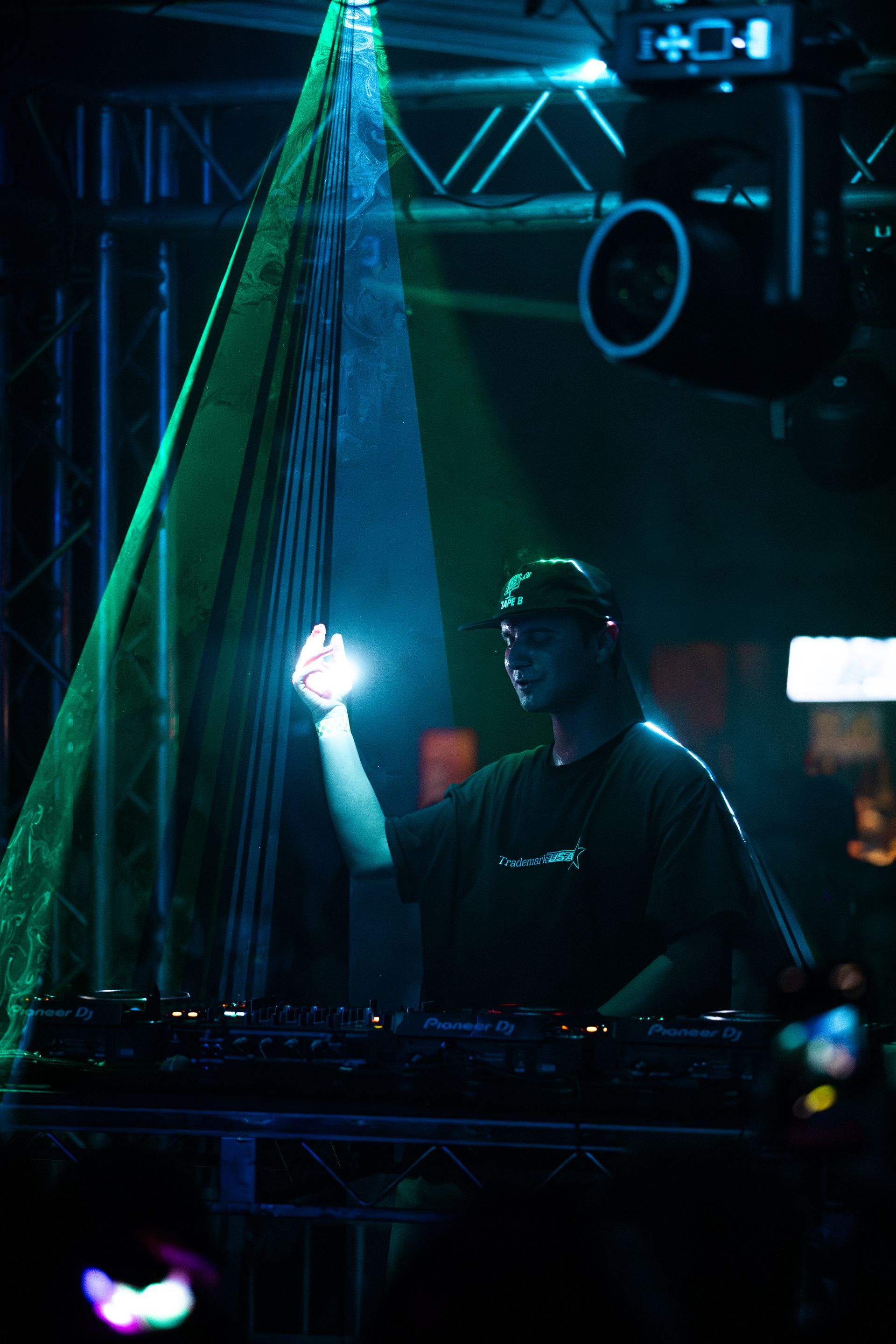 A dj is playing music in a dark room with a green light behind him