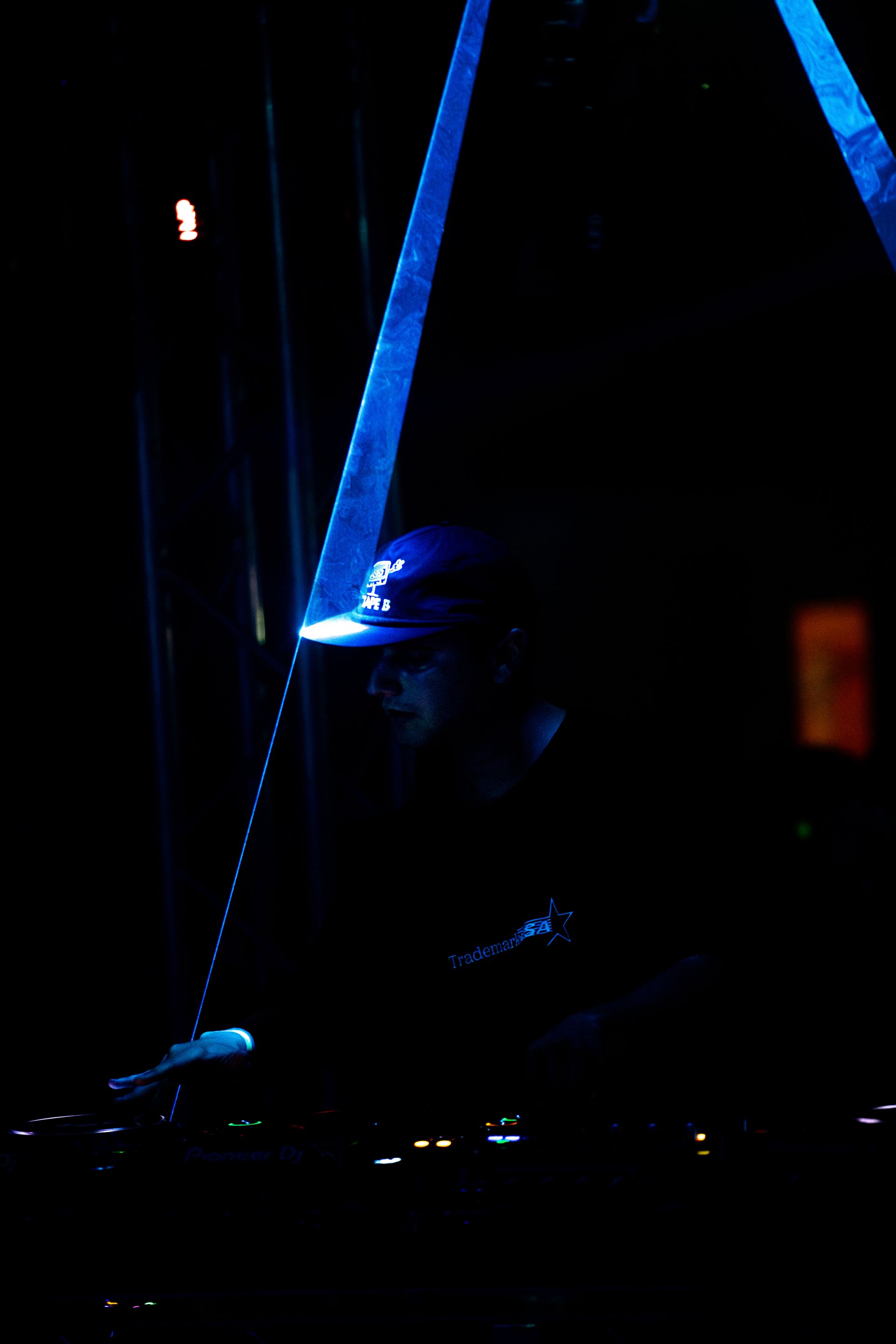A man in a hat is sitting in a dark room with a blue light behind him.