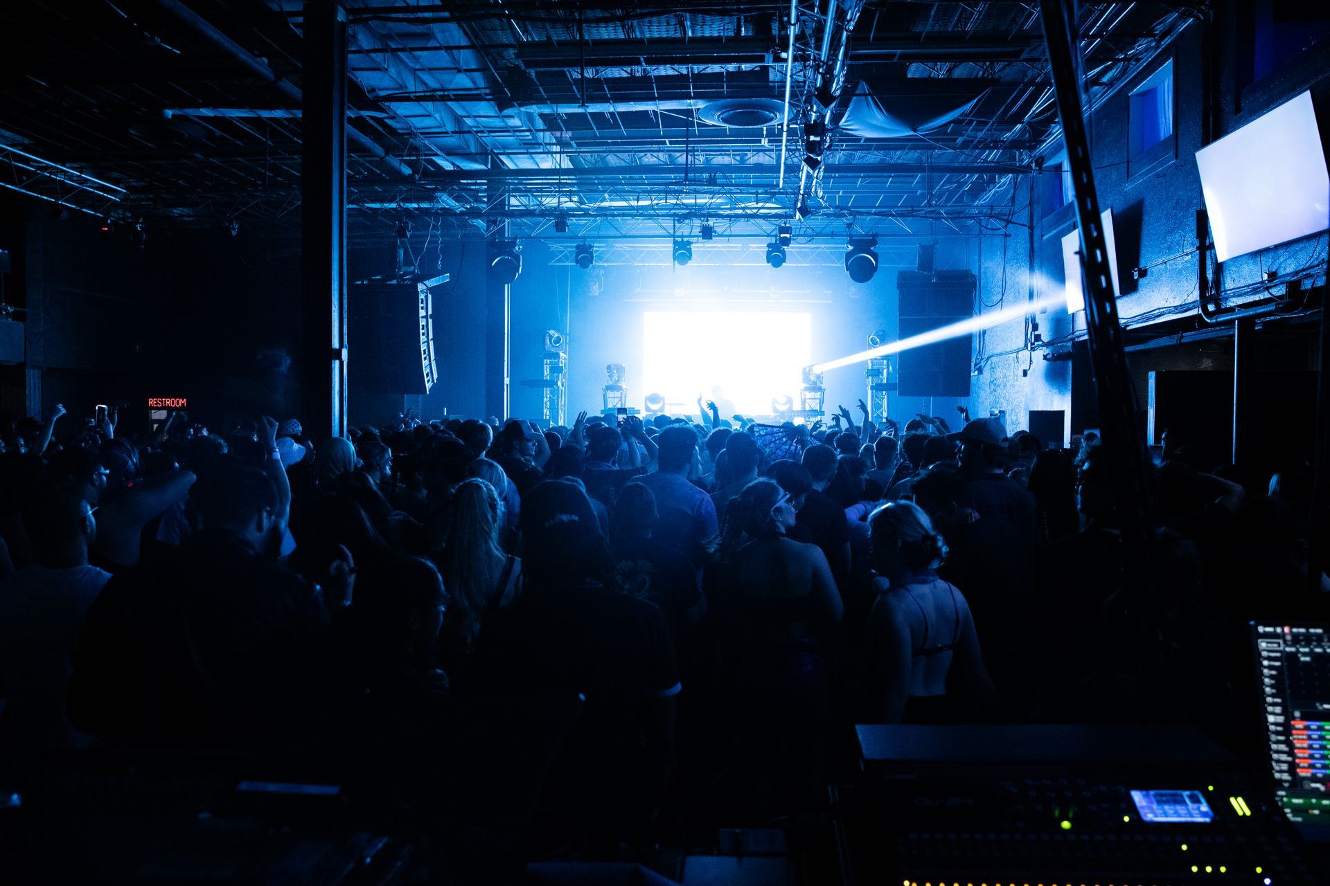 A crowd of people are gathered in a dark room at a concert.