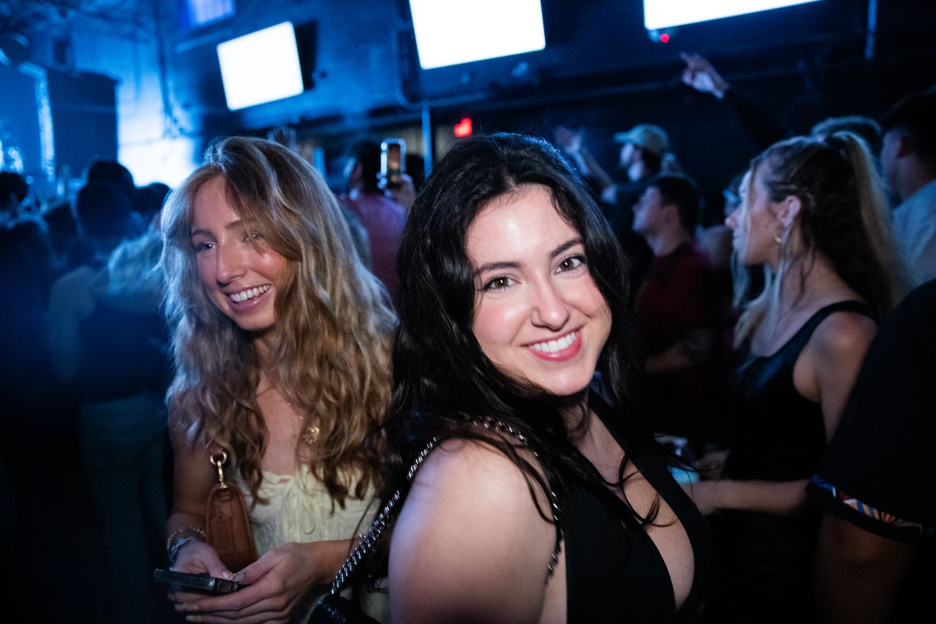 Two women are posing for a picture in a crowded nightclub.