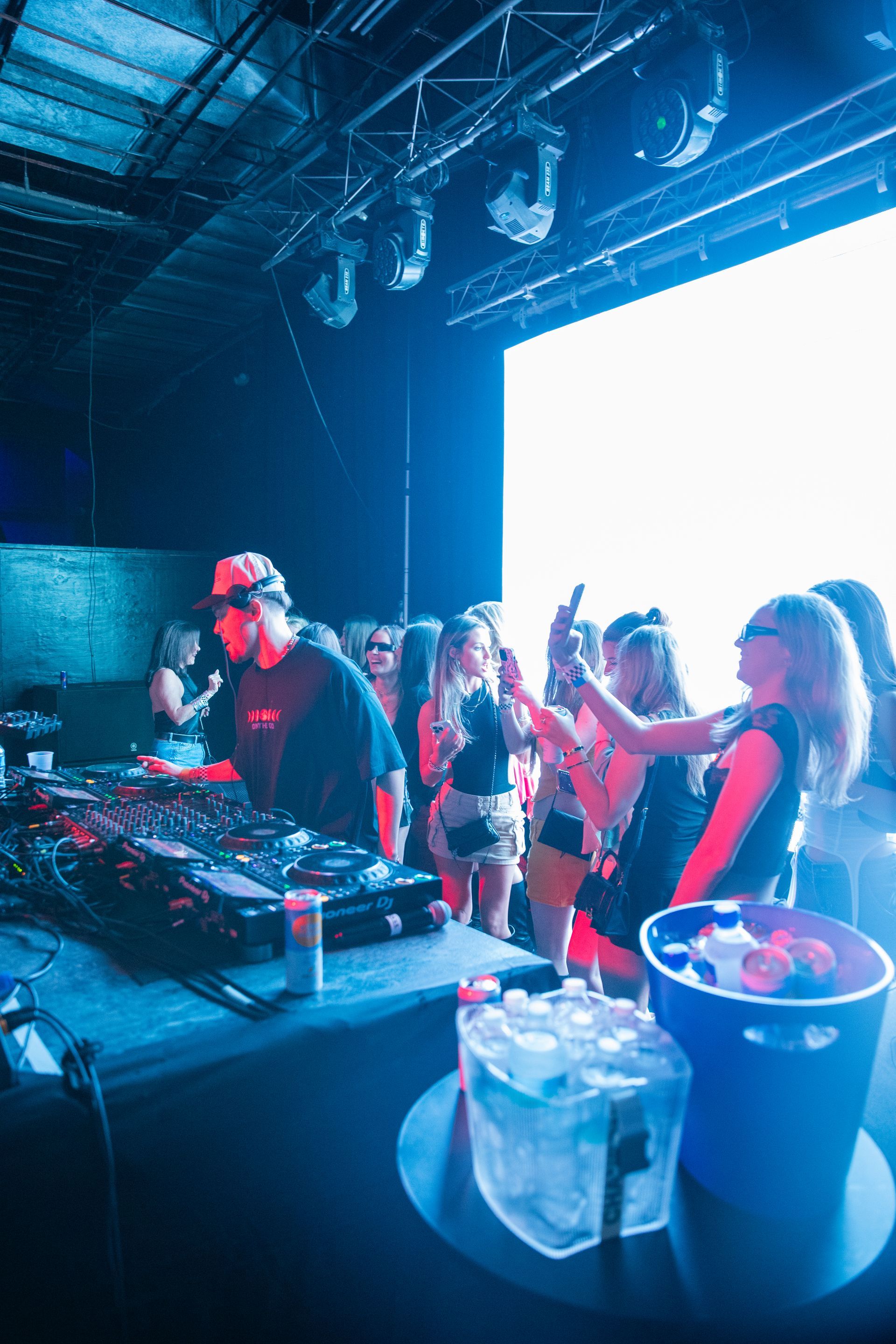 A group of people are standing around a dj in a club.