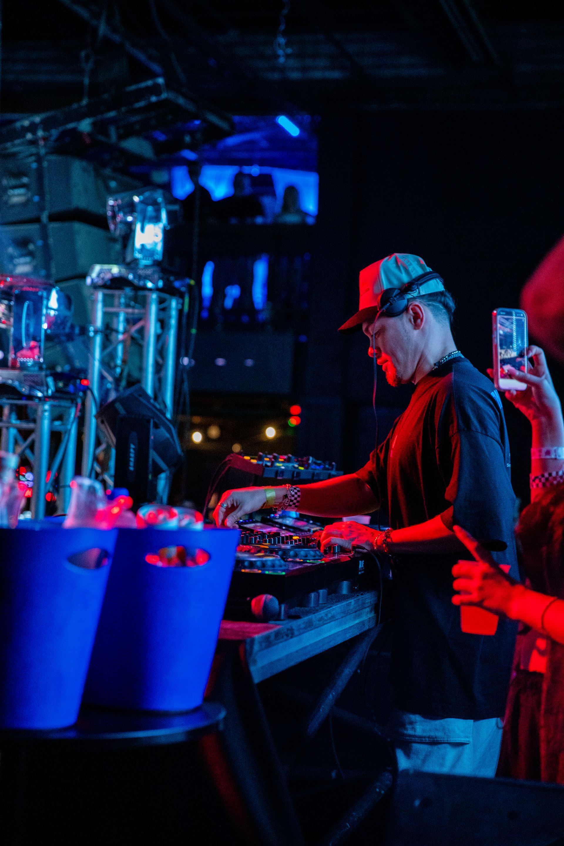 A man is playing a dj set in a dark room while a woman takes a picture of him.