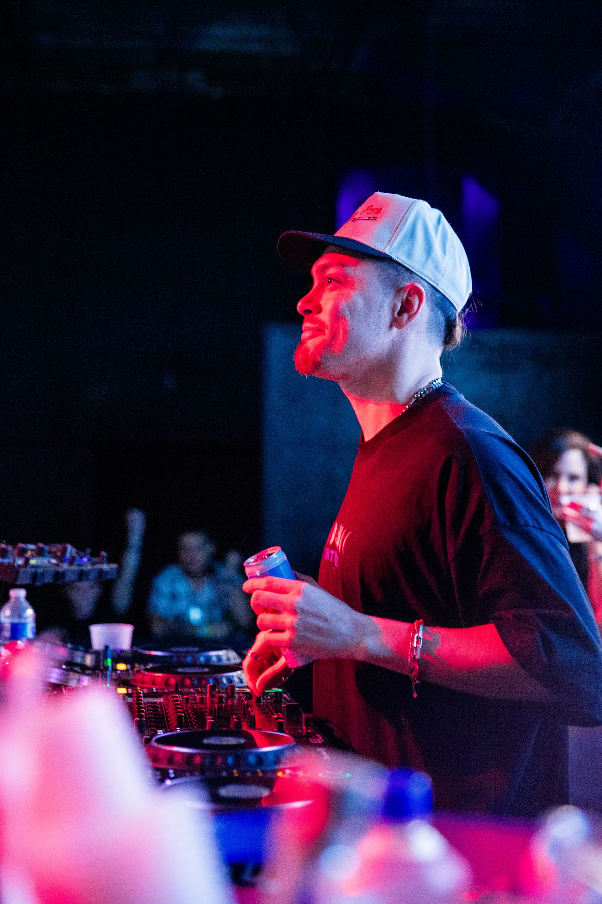 A man in a hat is standing in a dark room holding a drink.