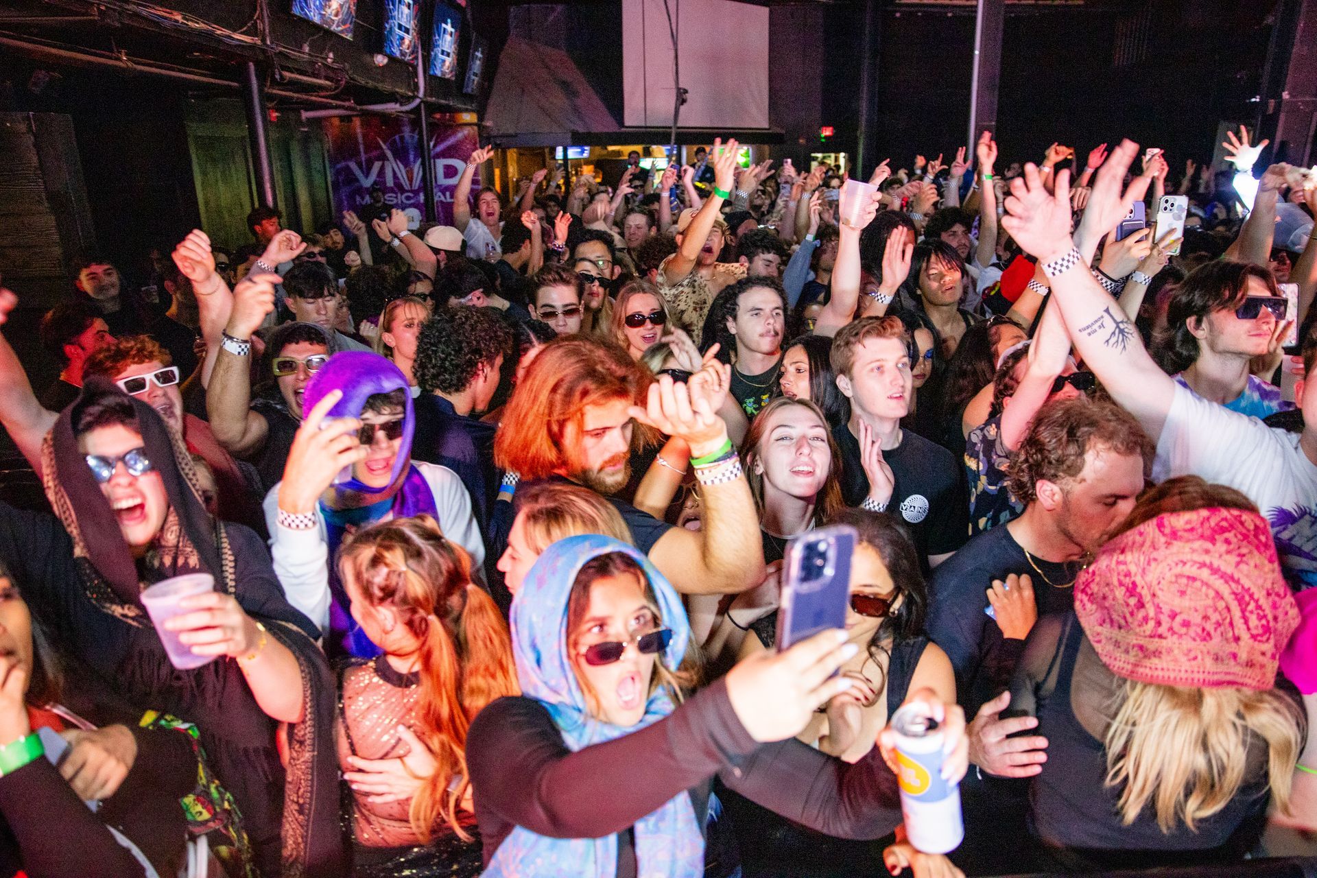A crowd of people are dancing and taking pictures at a party.