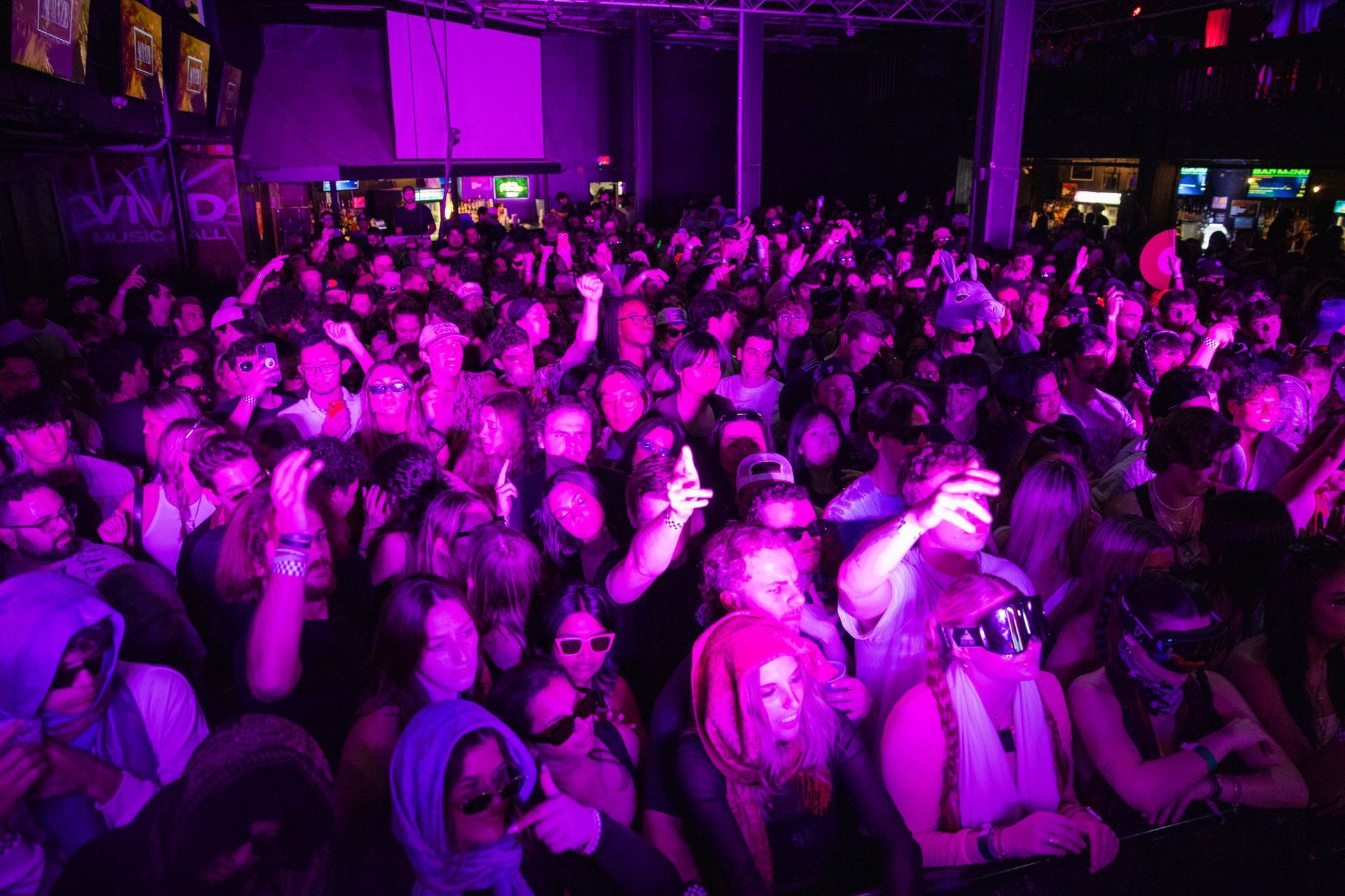 A crowd of people are standing in a dark room with purple lights.
