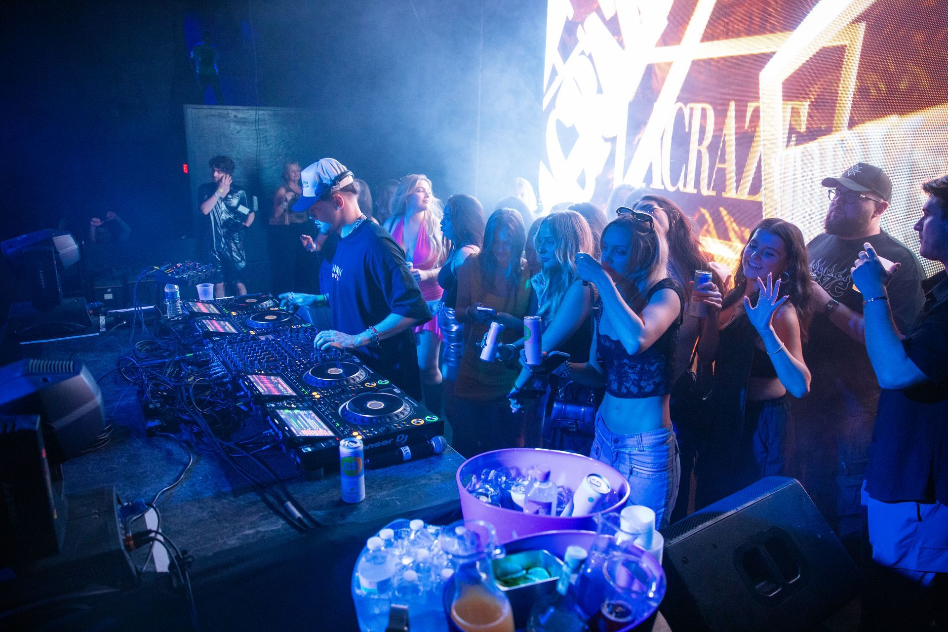 A group of people are standing around a dj at a party.