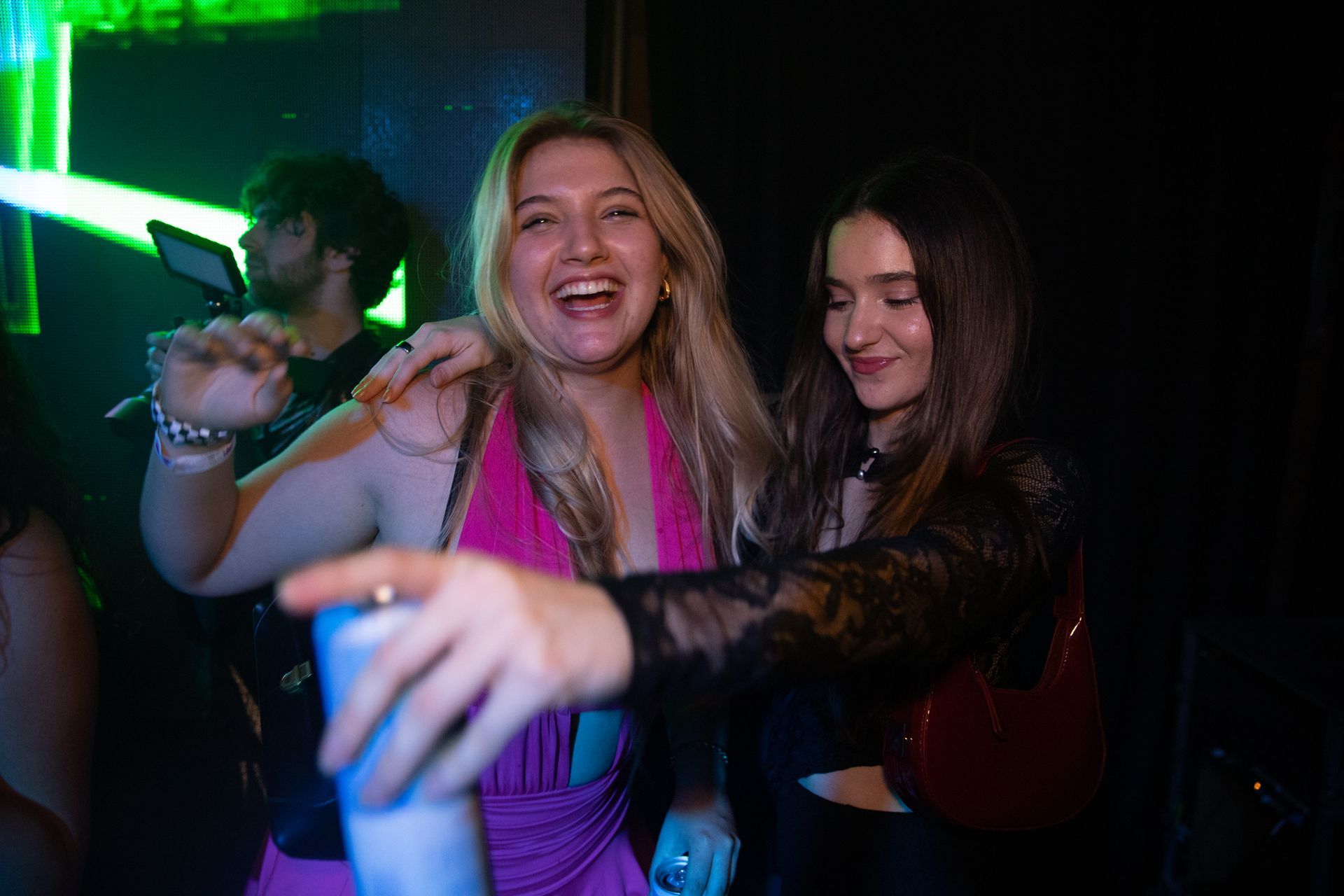 Two women are dancing in a club and one is holding a cup.