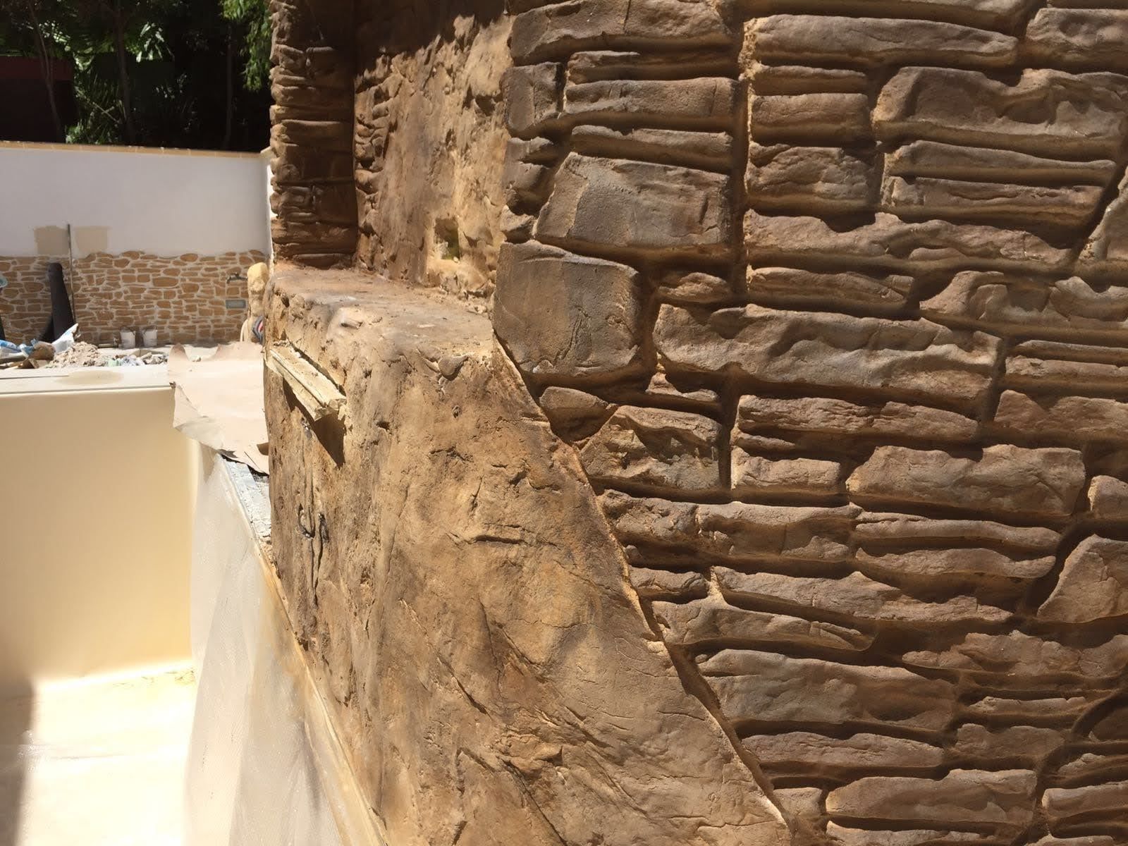 Un primo piano di un muro di pietra con una piscina sullo sfondo