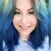 A person with shoulder-length, ombre blue hair and a light blue shirt smiling at the camera.